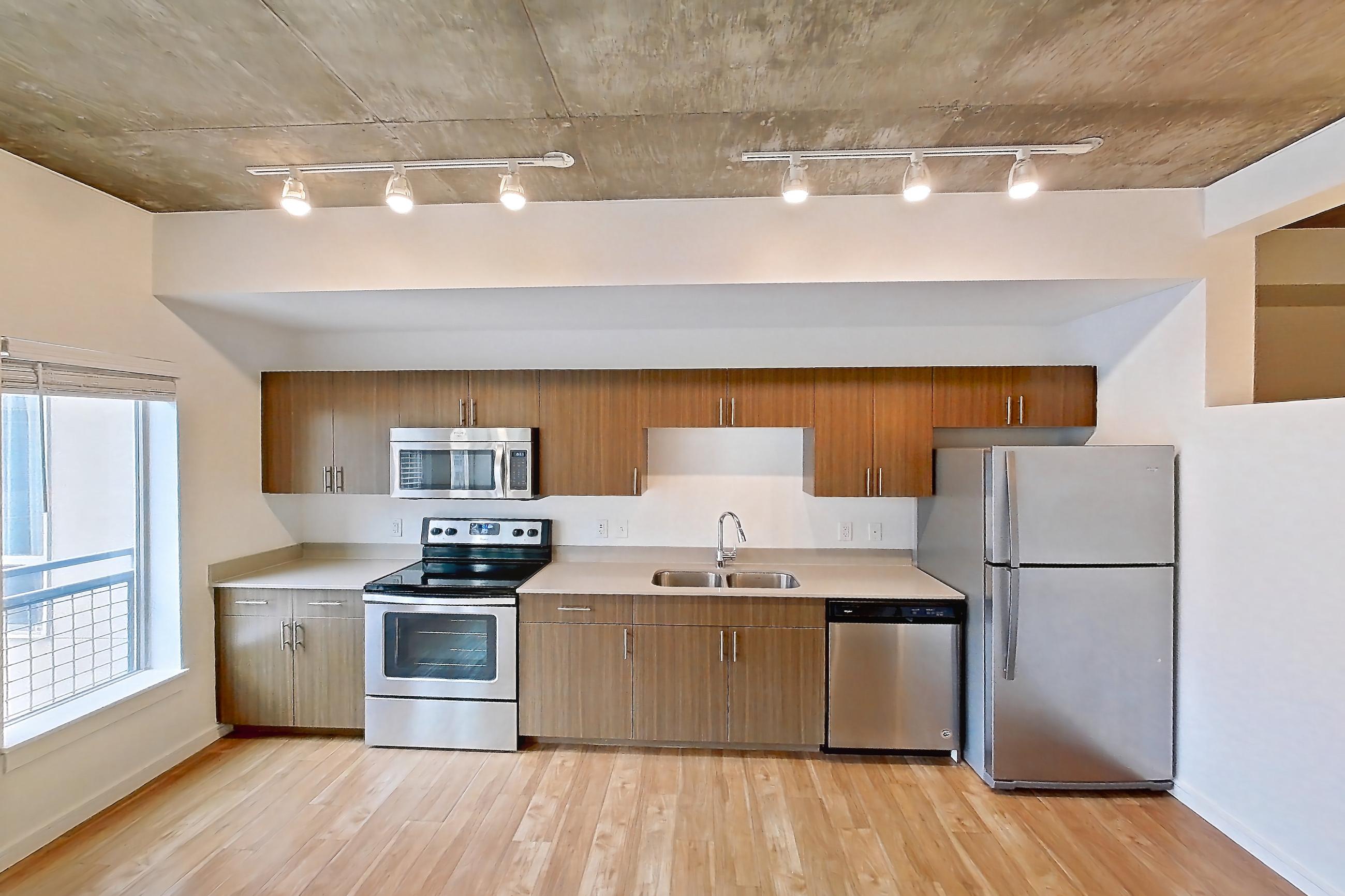 Living space with dishwasher, electric range, light countertops, light wood-finish flooring, microwave, oven/range, refrigerator, and stainless steel appliances, Apartment 1013 at Cadence at Union Station