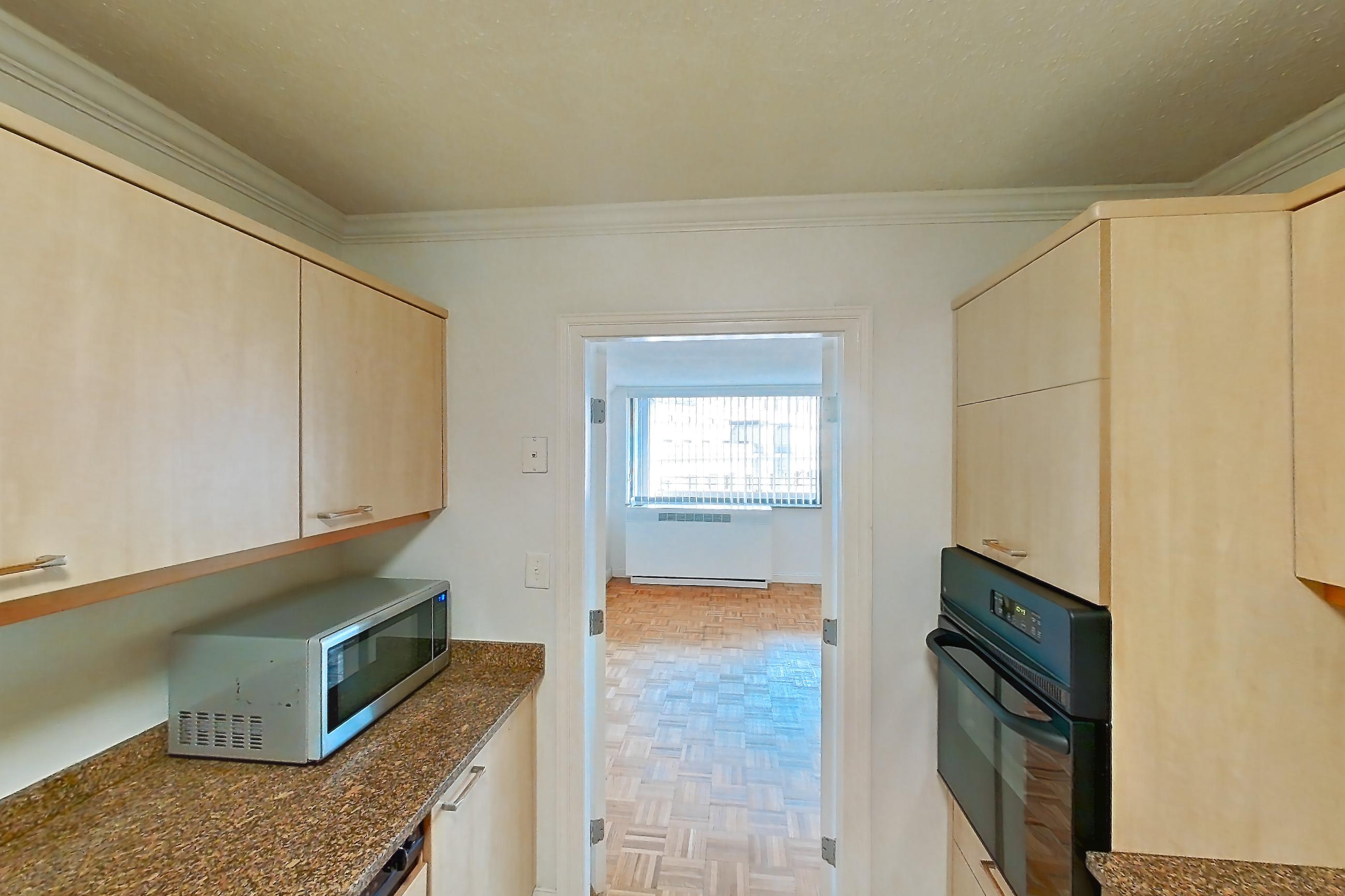 Kitchen with black appliances, cooktop, dark stone countertops, electric cooktop, light tile flooring, microwave, oven/range, and stainless steel appliances, Apartment 221-0618 at Church Park