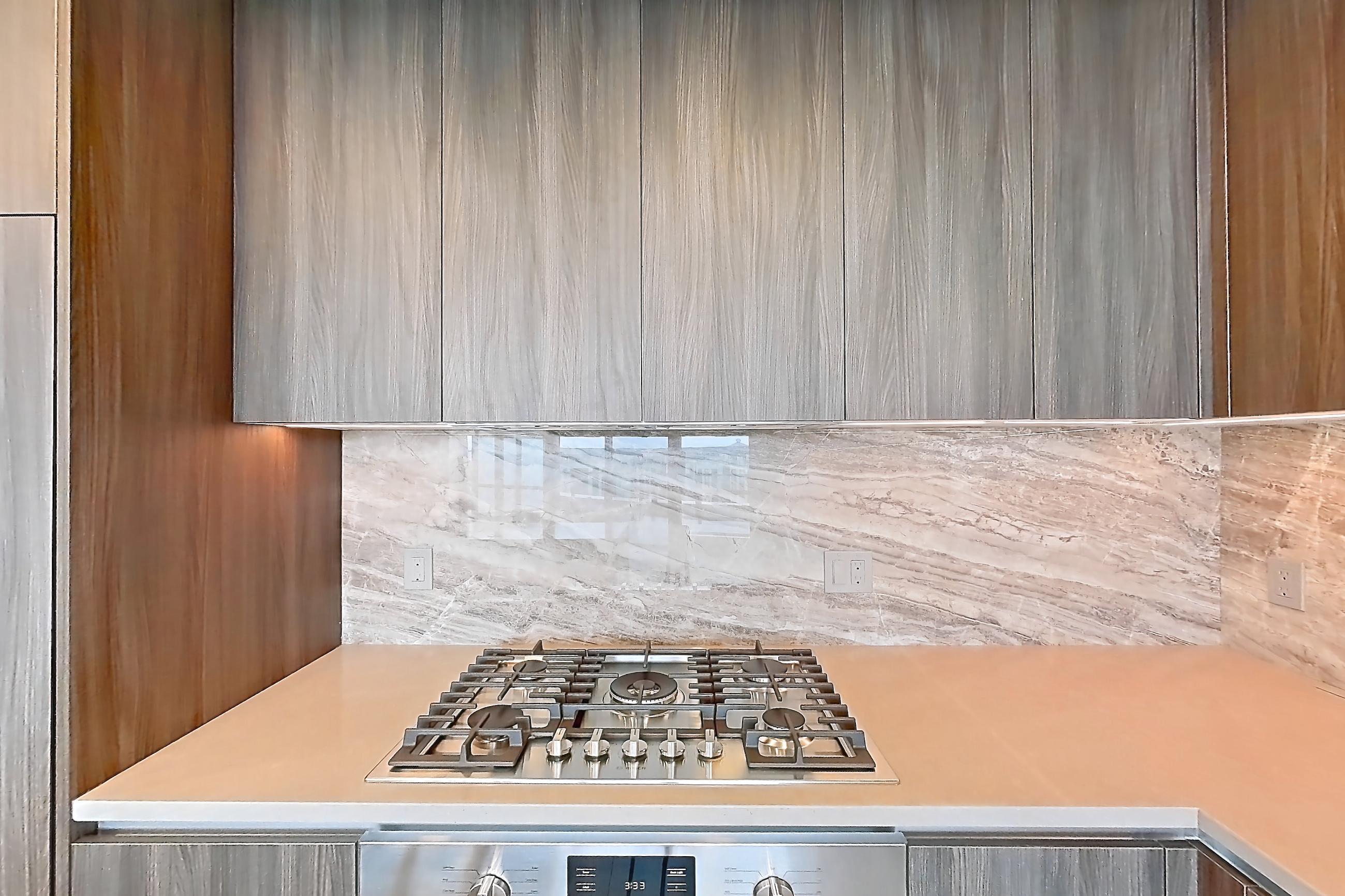 Kitchen with cooktop, gas cooktop, light stone countertops, light wood-finish flooring, oven/range, and stainless steel appliances, Apartment 1712 at Zephyr