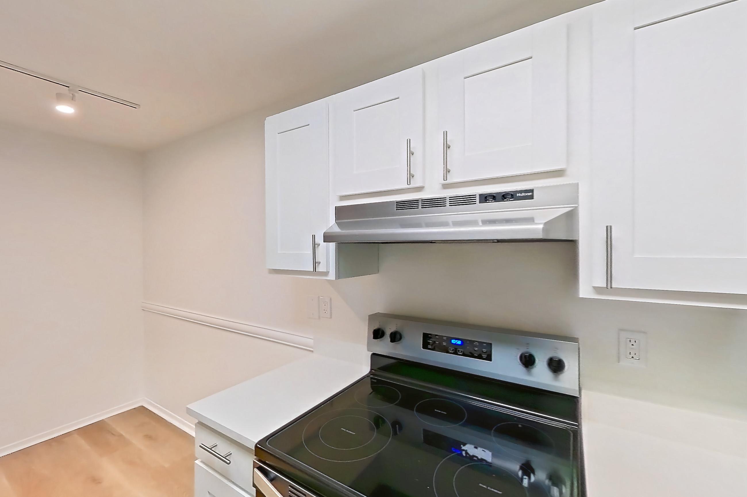 Kitchen with dishwasher, electric range, in-unit laundry, light countertops, light wood-finish flooring, oven/range, range hood, refrigerator, and stainless steel appliances, Apartment 08S at James Pointe