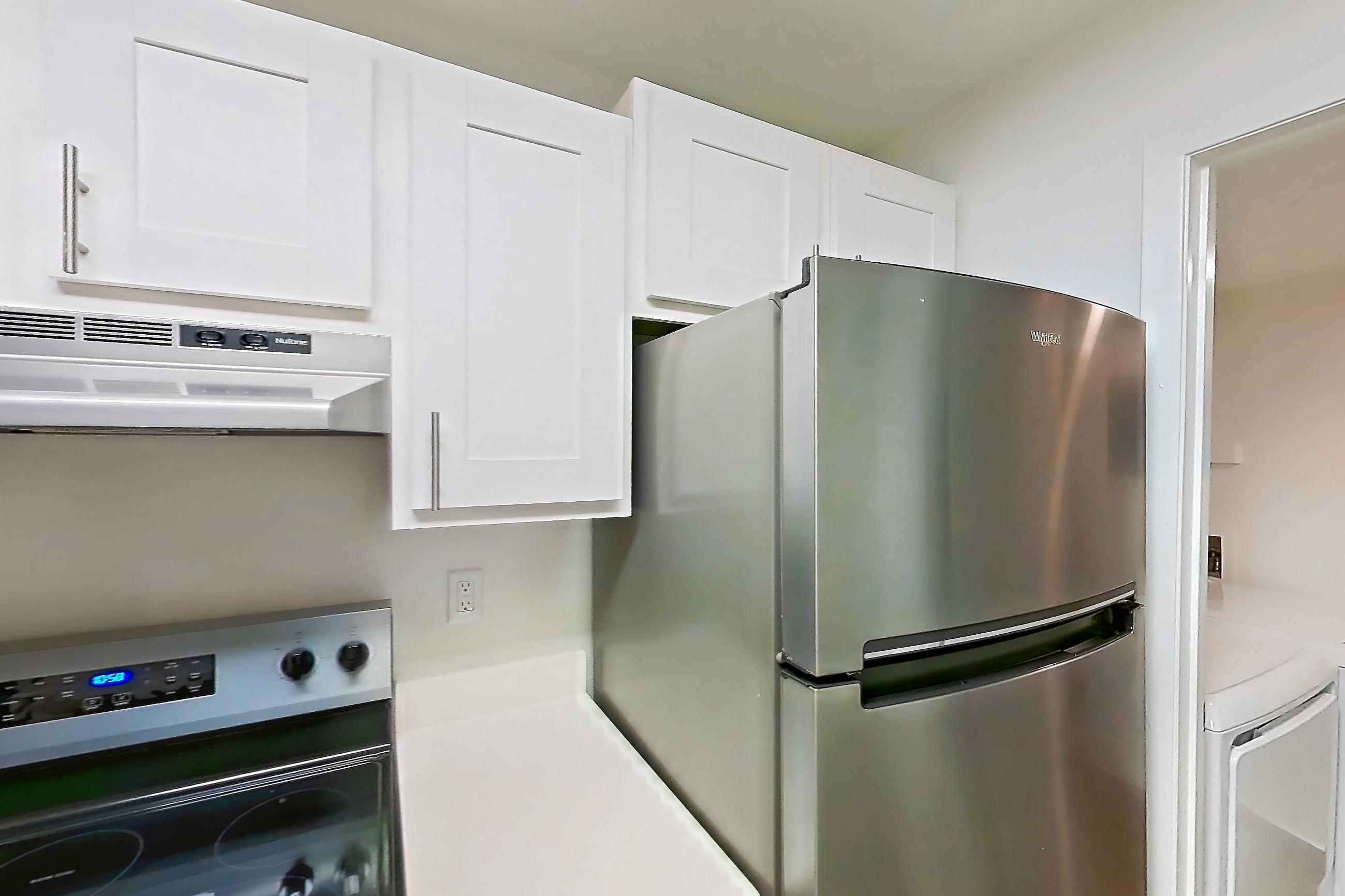 Kitchen with dishwasher, electric range, in-unit laundry, light countertops, light wood-finish flooring, oven/range, range hood, refrigerator, and stainless steel appliances, Apartment 08S at James Pointe