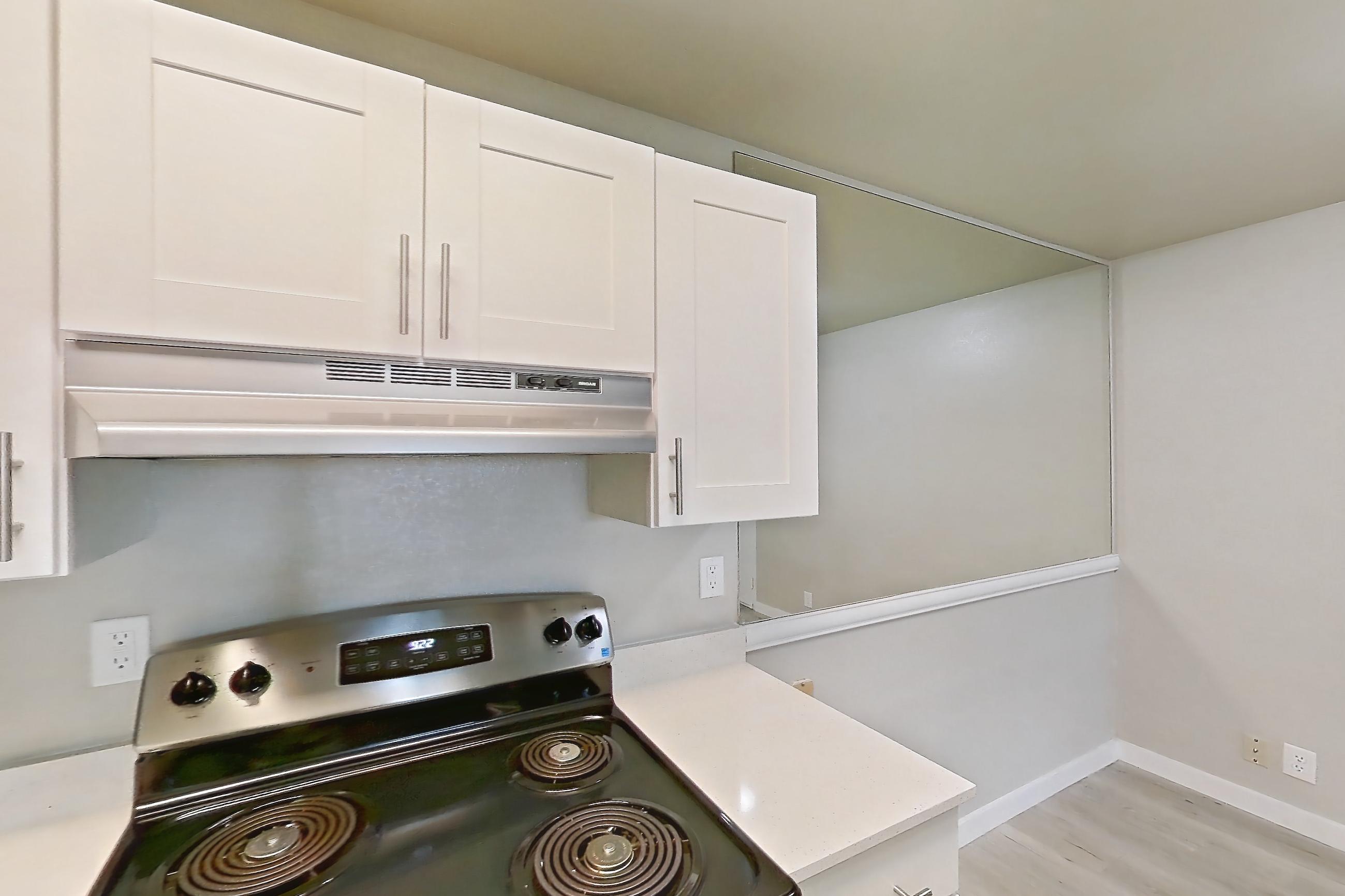 Kitchen with dishwasher, electric range, in-unit laundry, light countertops, light stone countertops, light wood-finish flooring, oven/range, range hood, refrigerator, and stainless steel appliances, Apartment 02H at James Pointe