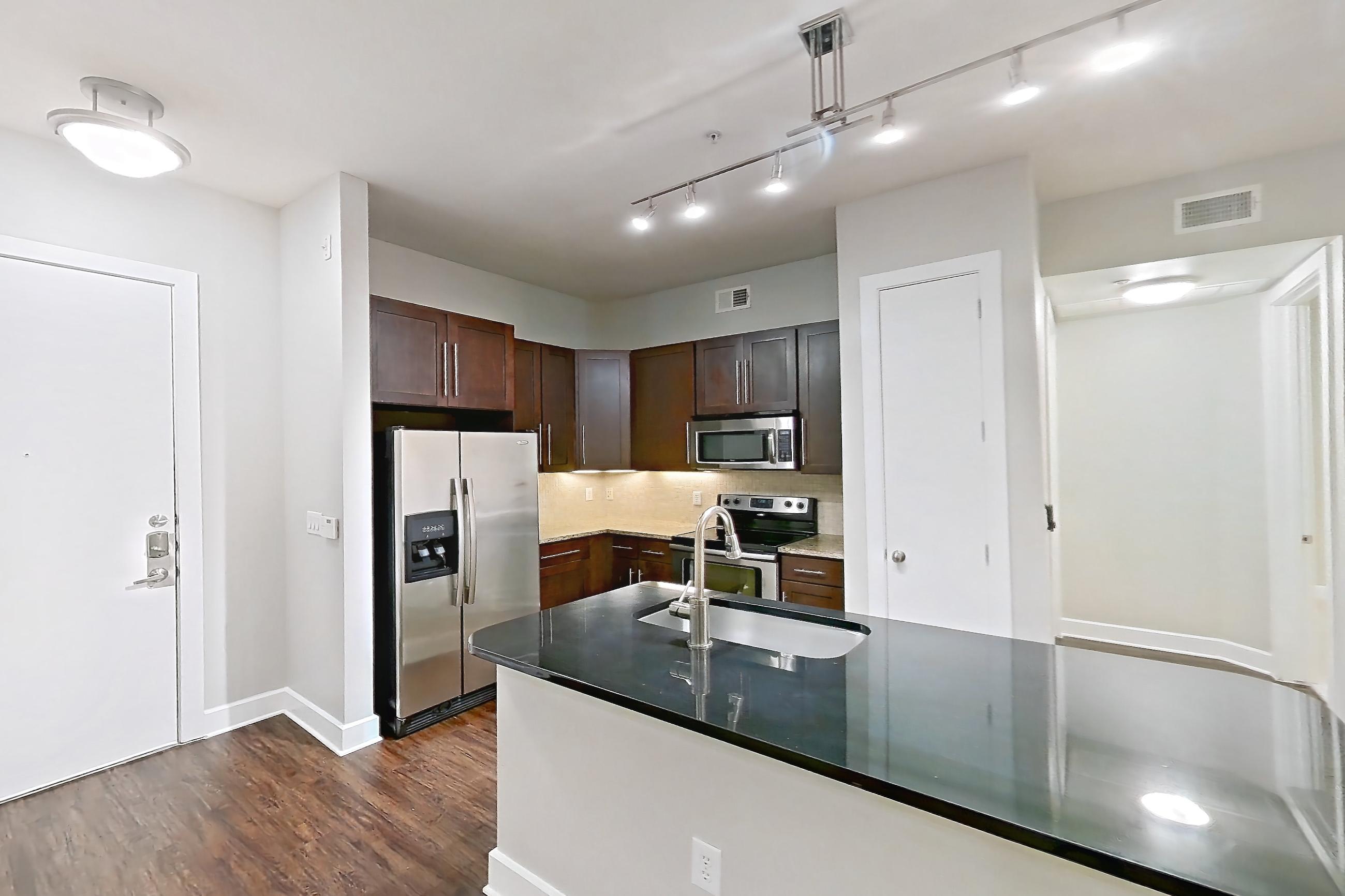 Living space with dark stone countertops, dark wood-finish flooring, electric range, kitchen island, light countertops, light stone countertops, oven/range, refrigerator, and stainless steel appliances, Apartment 179 at Domain at CityCentre