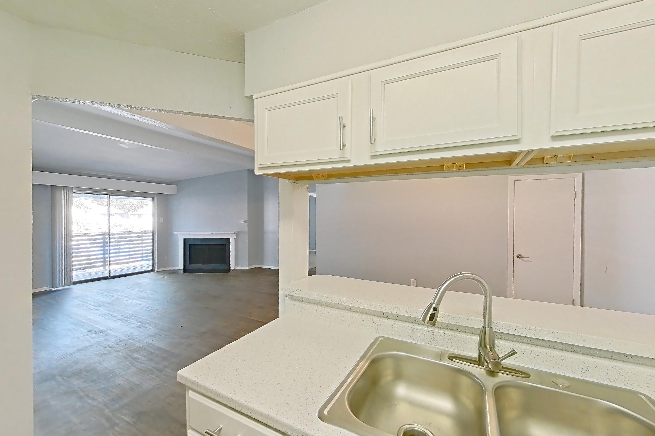 Kitchen with black appliances, dark wood-finish flooring, dishwasher, electric range, fireplace, light countertops, light stone countertops, light wood-finish flooring, oven/range, and refrigerator, Apartment 190 at Eleven600 Apartments