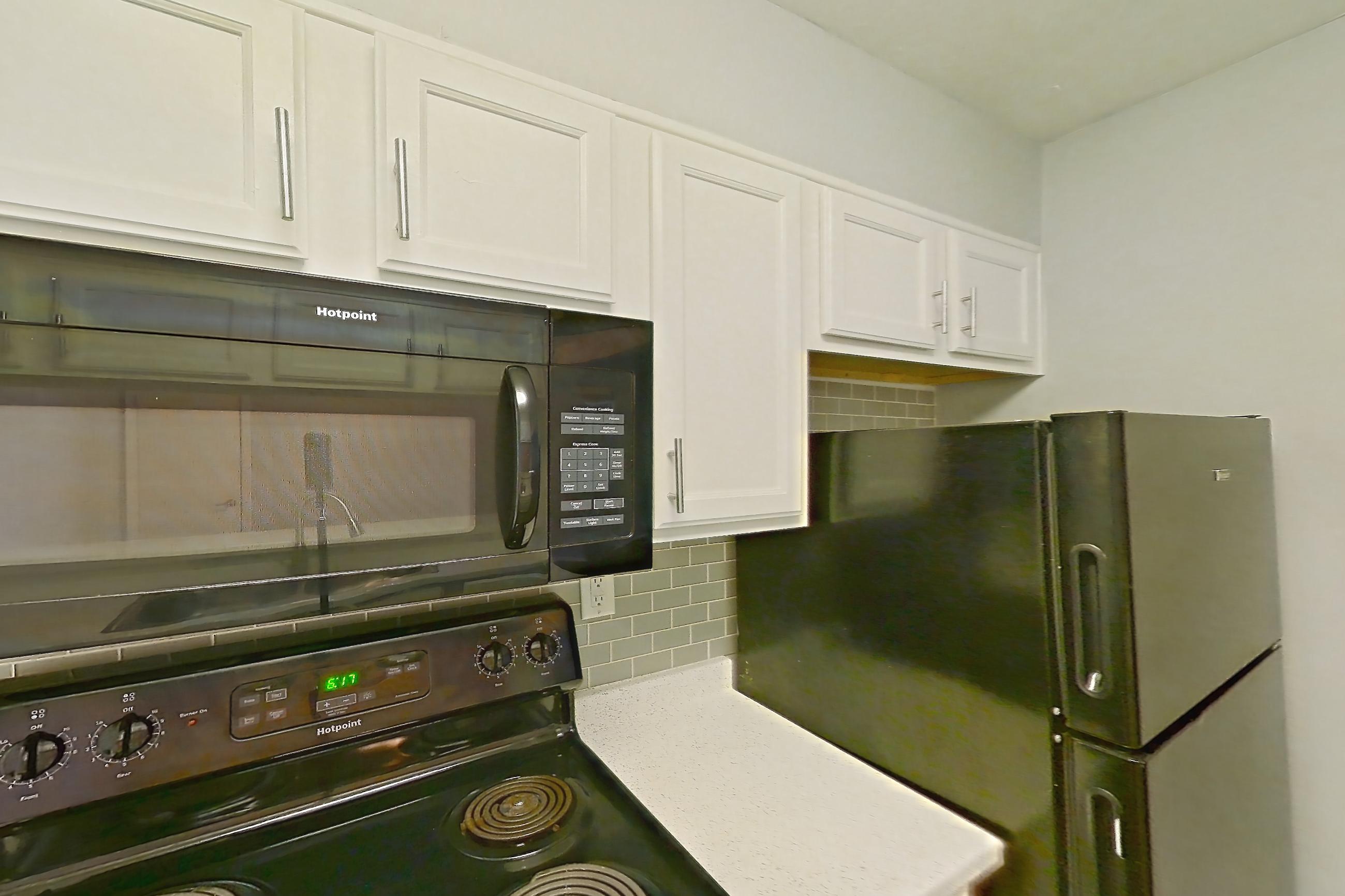 Kitchen with black appliances, dark wood-finish flooring, dishwasher, electric range, fireplace, light countertops, light stone countertops, light wood-finish flooring, oven/range, and refrigerator, Apartment 190 at Eleven600 Apartments