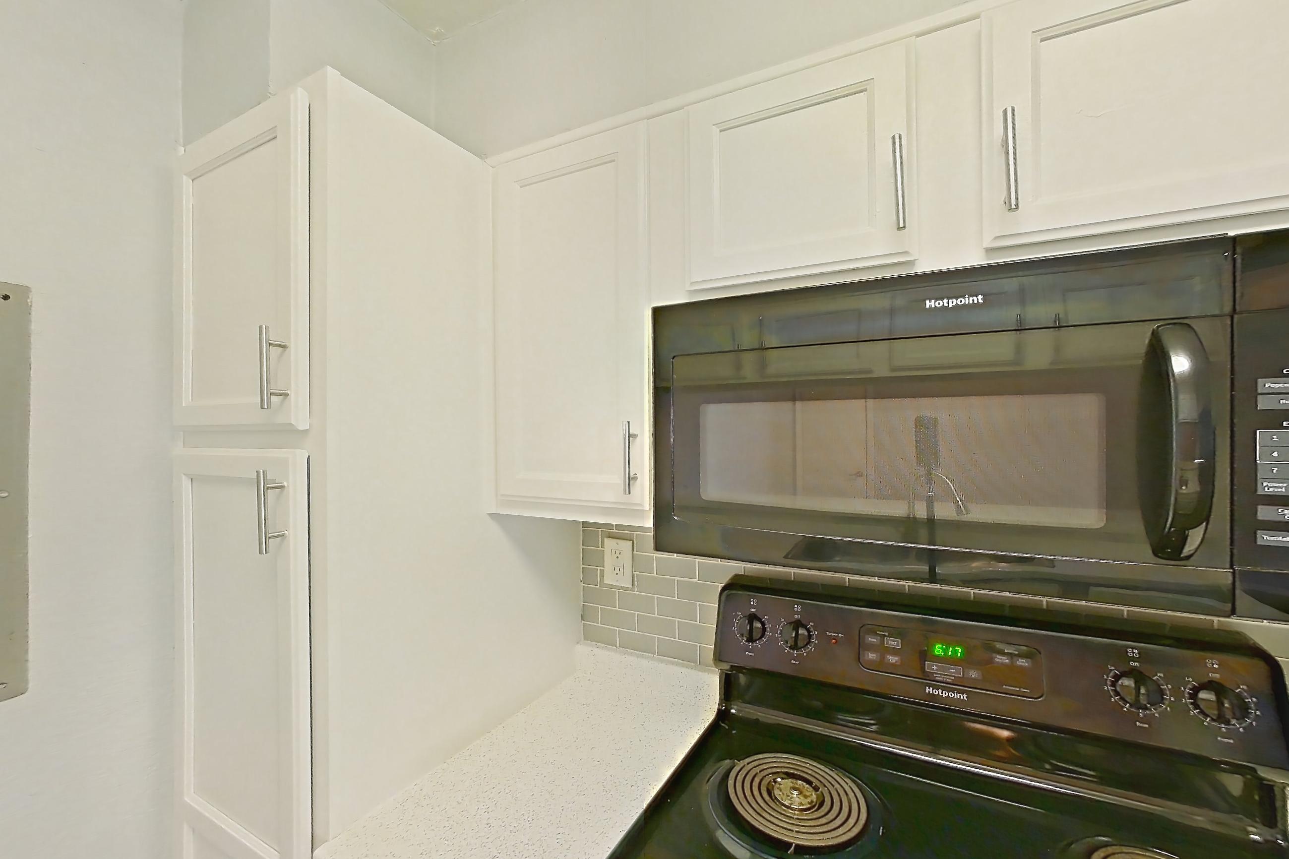Kitchen with black appliances, dark wood-finish flooring, dishwasher, electric range, fireplace, light countertops, light stone countertops, light wood-finish flooring, oven/range, and refrigerator, Apartment 190 at Eleven600 Apartments