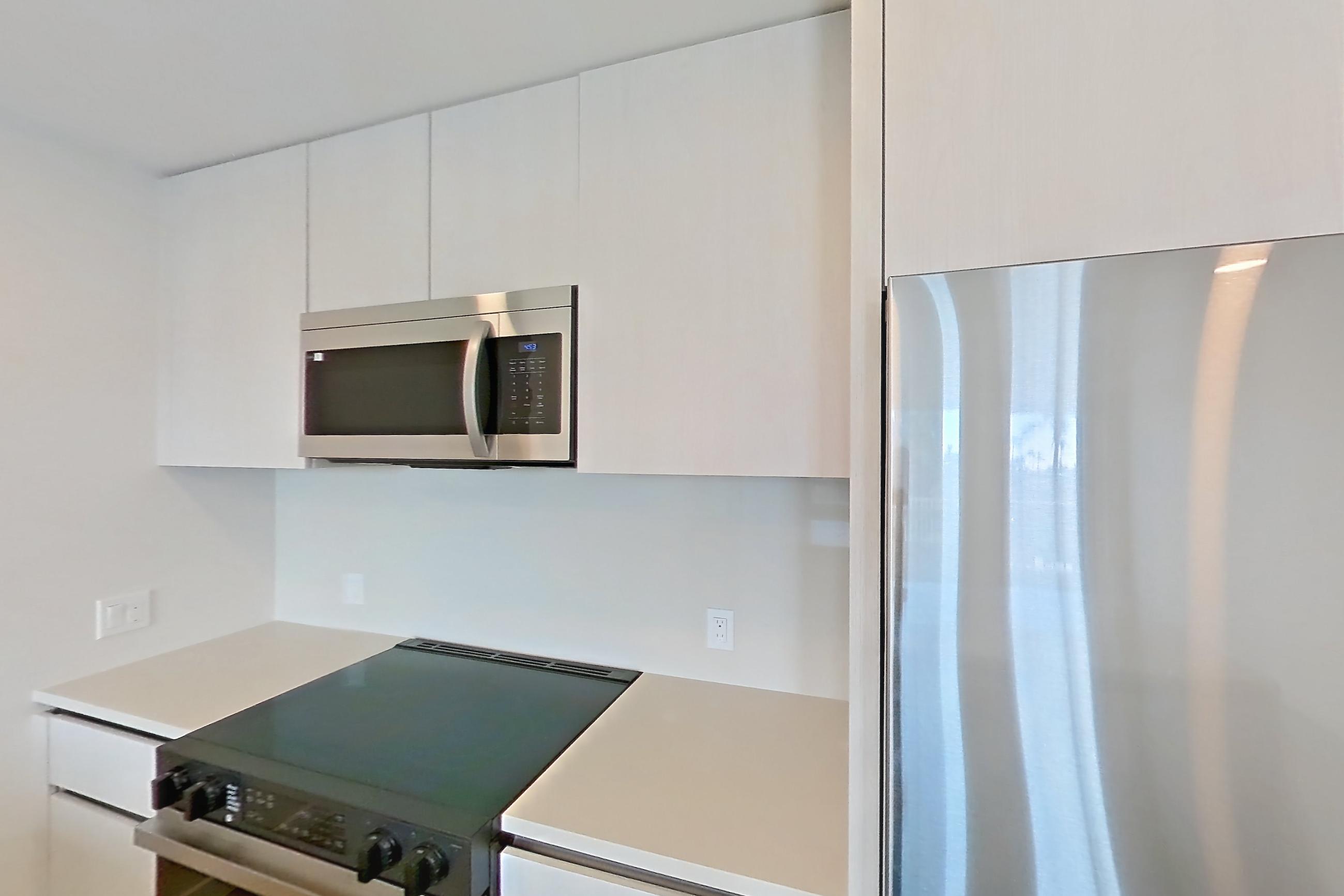 Kitchen with black appliances, dishwasher, electric range, light countertops, light stone countertops, light wood-finish flooring, microwave, oven/range, refrigerator, and stainless steel appliances, Apartment 342 at Rowyn