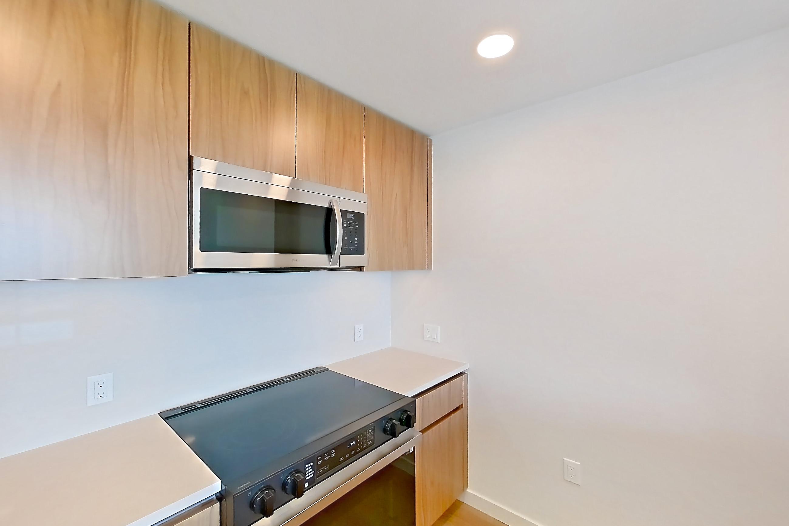 Kitchen with dishwasher, electric range, light countertops, light stone countertops, light wood-finish flooring, microwave, oven/range, refrigerator, and stainless steel appliances, Apartment 410 at Rowyn
