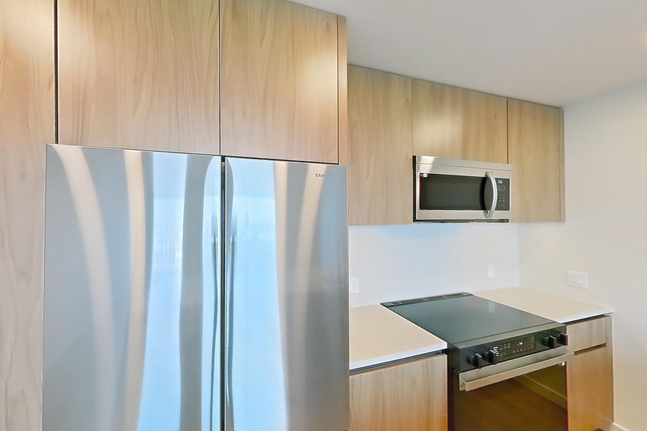 Kitchen with dishwasher, electric range, light countertops, light wood-finish flooring, microwave, oven/range, refrigerator, and stainless steel appliances, Apartment 610 at Rowyn