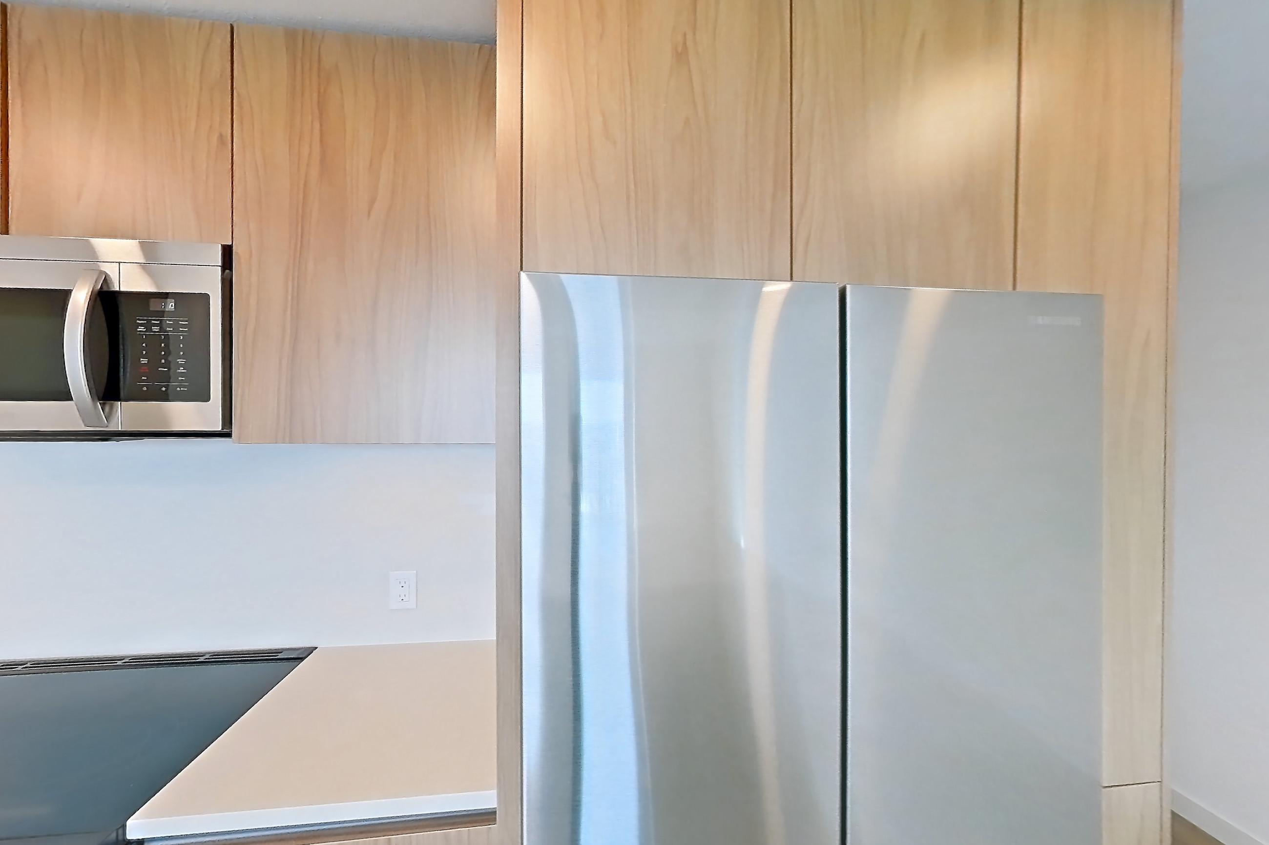 Kitchen with dishwasher, electric range, light countertops, light stone countertops, light wood-finish flooring, microwave, oven/range, refrigerator, and stainless steel appliances, Apartment 853 at Rowyn