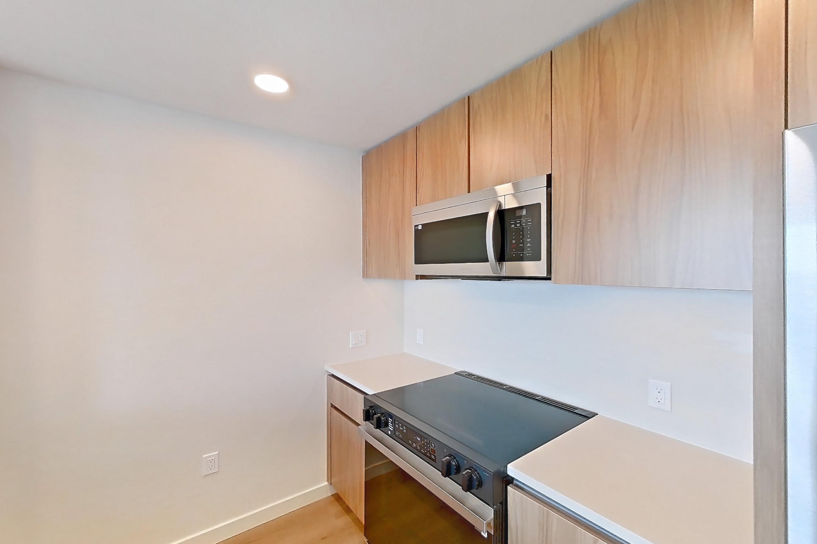 Kitchen with dishwasher, electric range, light countertops, light stone countertops, light wood-finish flooring, microwave, oven/range, refrigerator, and stainless steel appliances, Apartment 853 at Rowyn