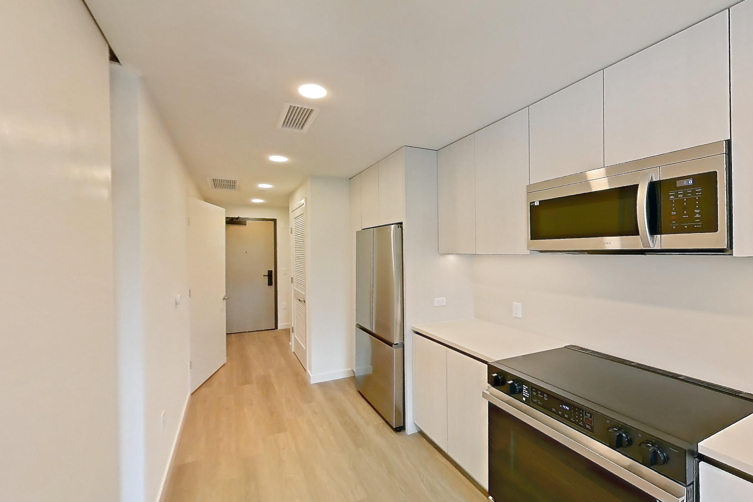 Kitchen with dishwasher, electric range, light countertops, light wood-finish flooring, microwave, oven/range, refrigerator, and stainless steel appliances, Apartment 303 at Rowyn