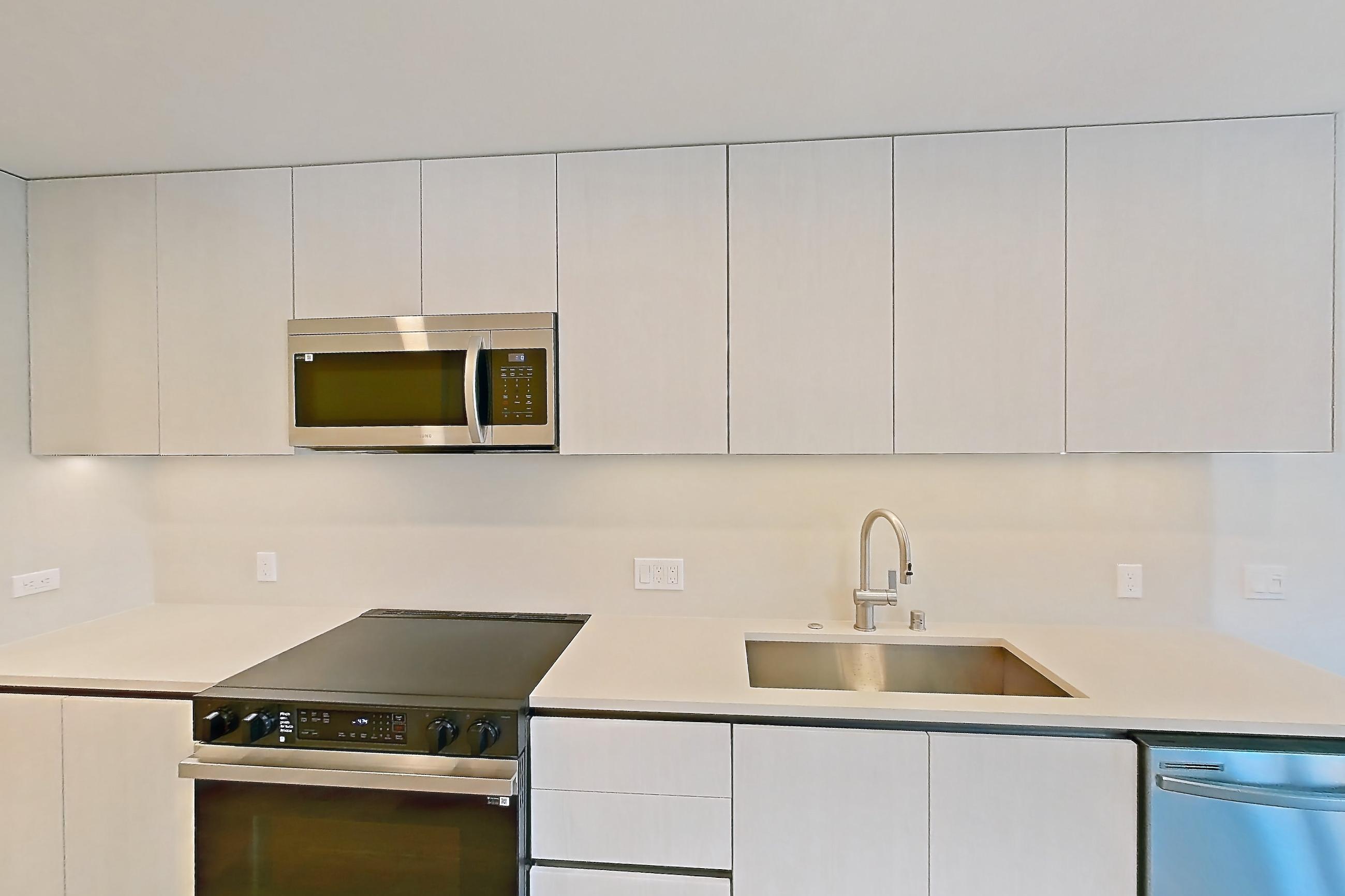 Kitchen with dishwasher, electric range, light countertops, light wood-finish flooring, microwave, oven/range, refrigerator, and stainless steel appliances, Apartment 303 at Rowyn