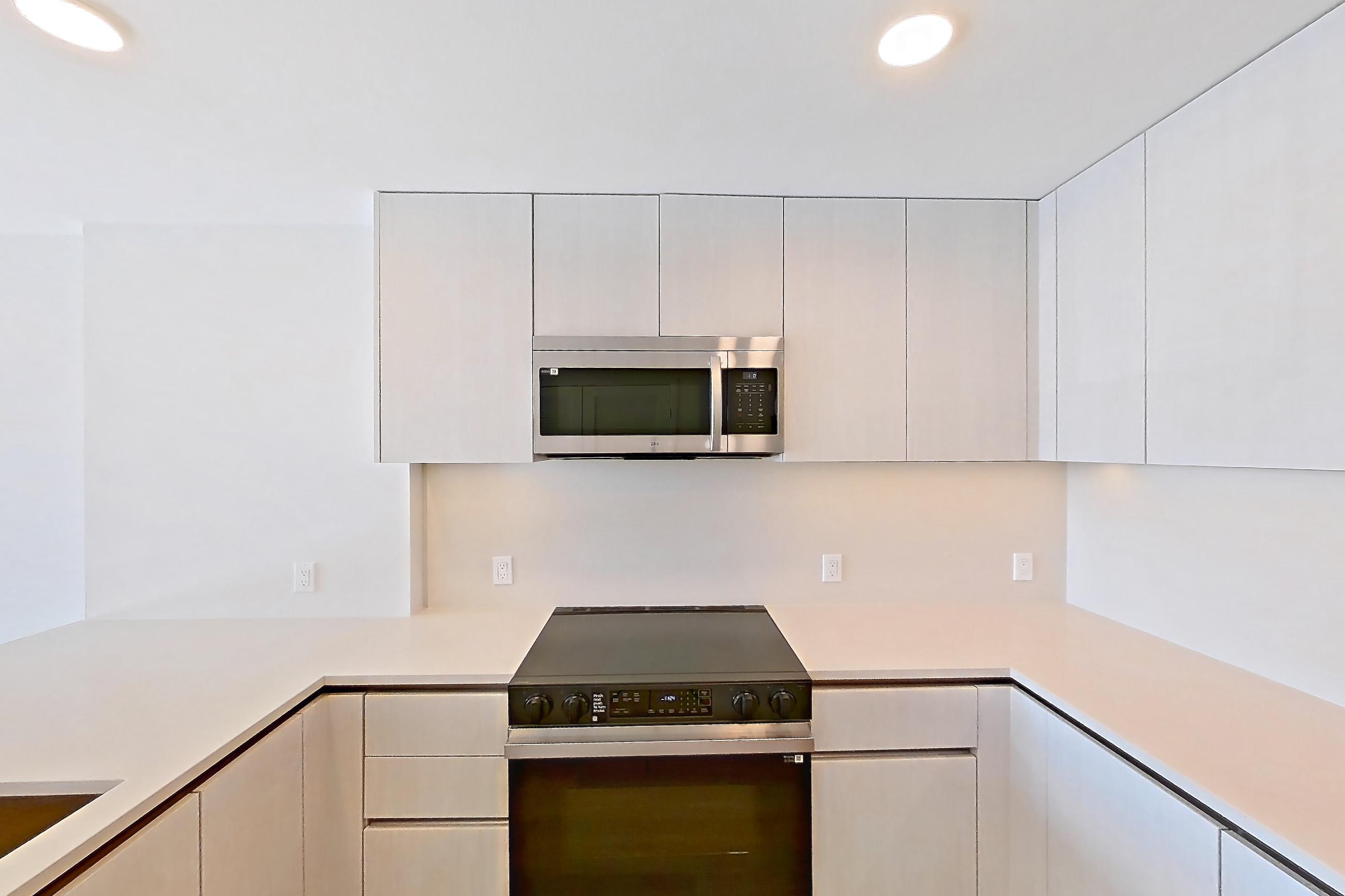 Kitchen with dishwasher, electric range, kitchen island, light countertops, light stone countertops, light wood-finish flooring, microwave, oven/range, refrigerator, and stainless steel appliances, Apartment 305 at Rowyn