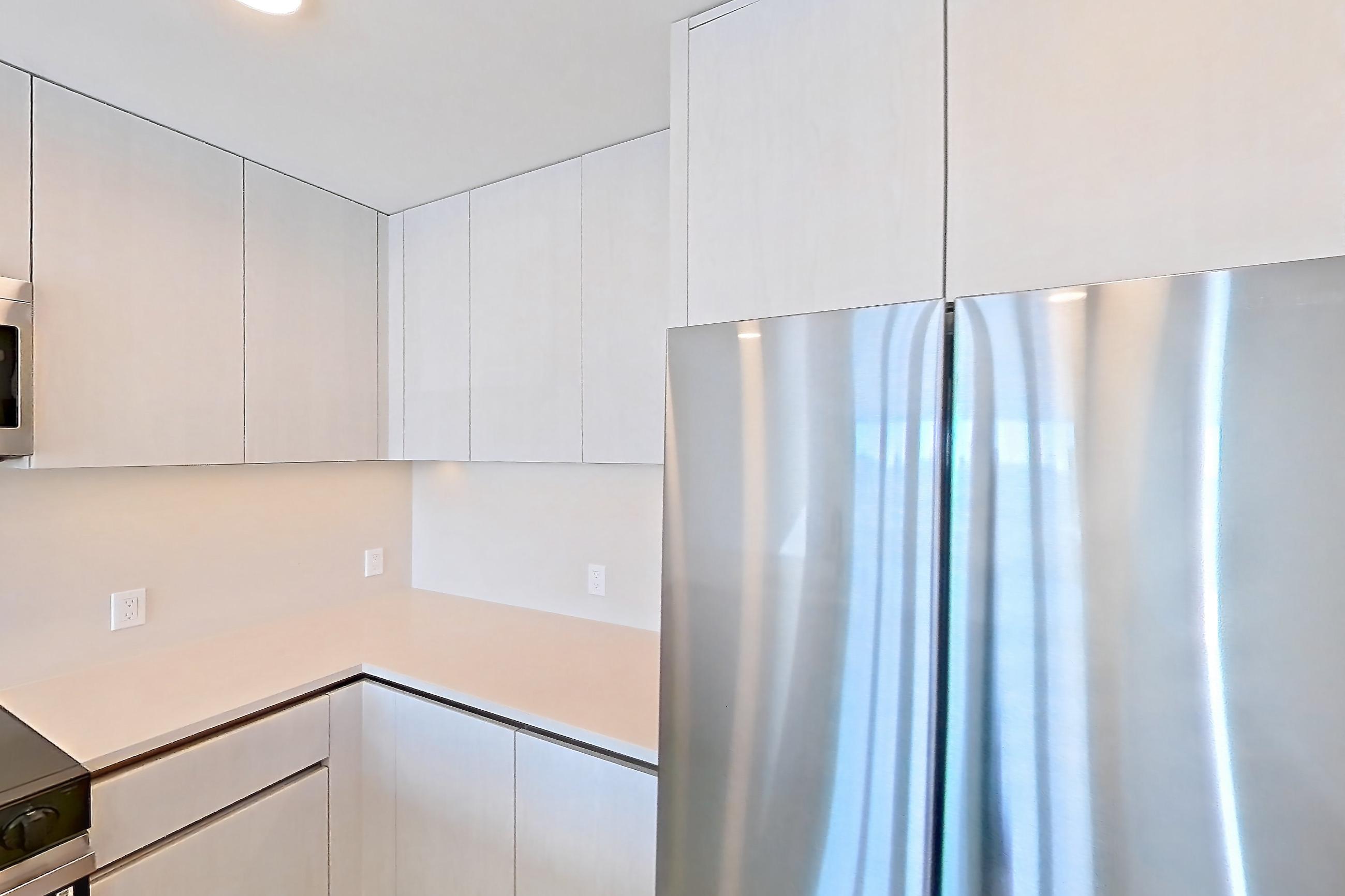 Kitchen with dishwasher, electric range, kitchen island, light countertops, light stone countertops, light wood-finish flooring, microwave, oven/range, refrigerator, and stainless steel appliances, Apartment 305 at Rowyn