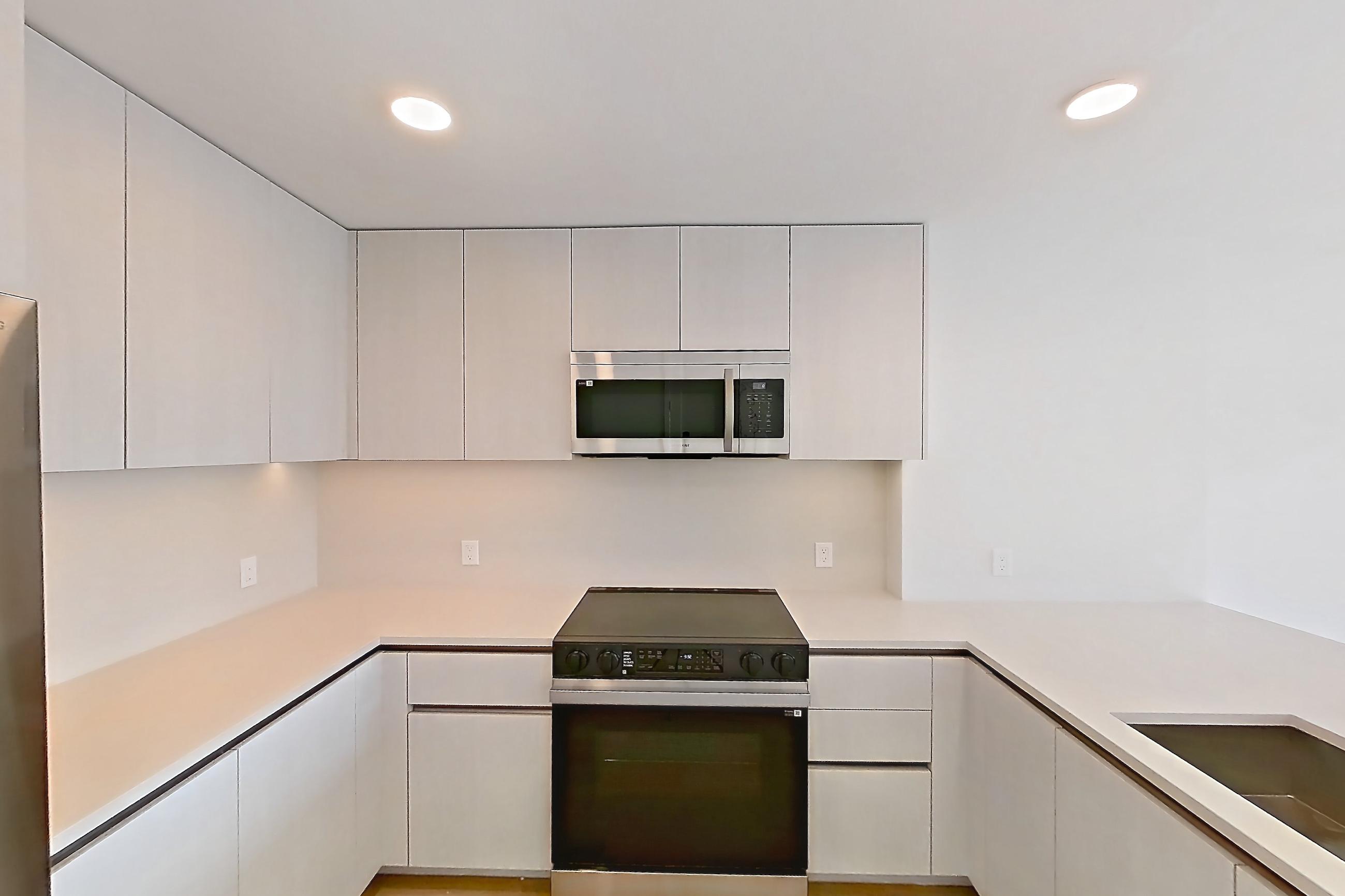 Kitchen with dishwasher, electric range, light countertops, light stone countertops, light wood-finish flooring, microwave, oven/range, refrigerator, and stainless steel appliances, Apartment 344 at Rowyn
