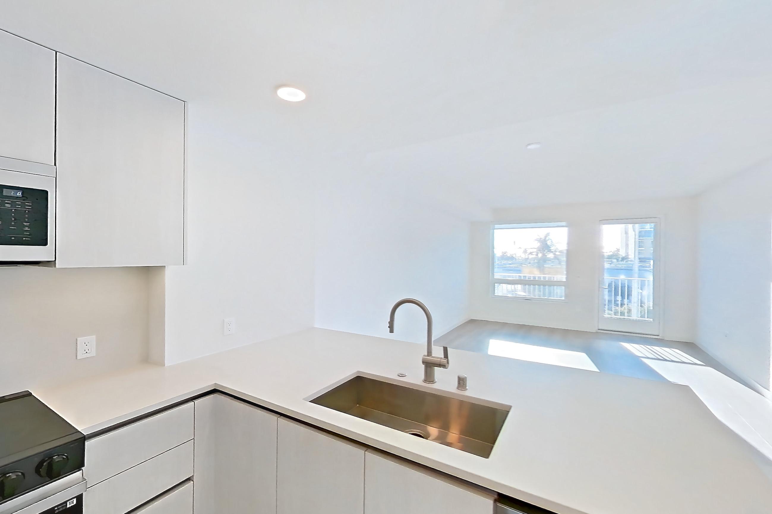 Kitchen with dishwasher, electric range, kitchen island, light countertops, light stone countertops, light wood-finish flooring, microwave, oven/range, refrigerator, and stainless steel appliances, Apartment 348 at Rowyn