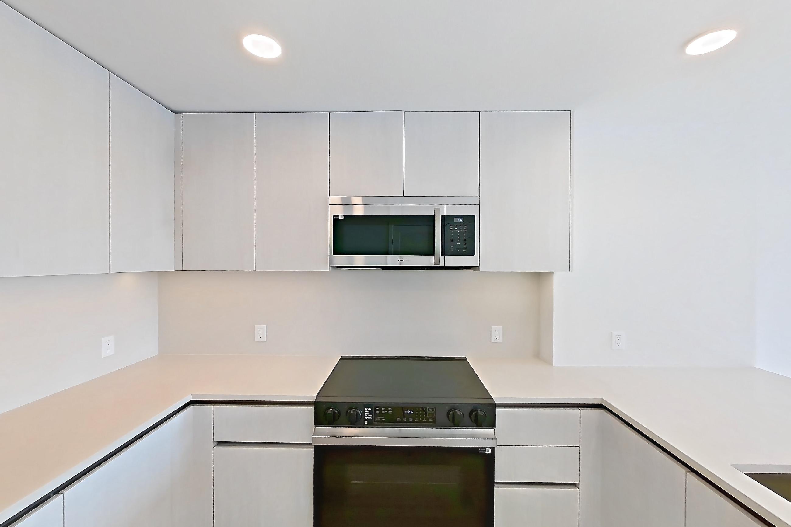 Kitchen with dishwasher, electric range, kitchen island, light countertops, light stone countertops, light wood-finish flooring, microwave, oven/range, refrigerator, and stainless steel appliances, Apartment 348 at Rowyn