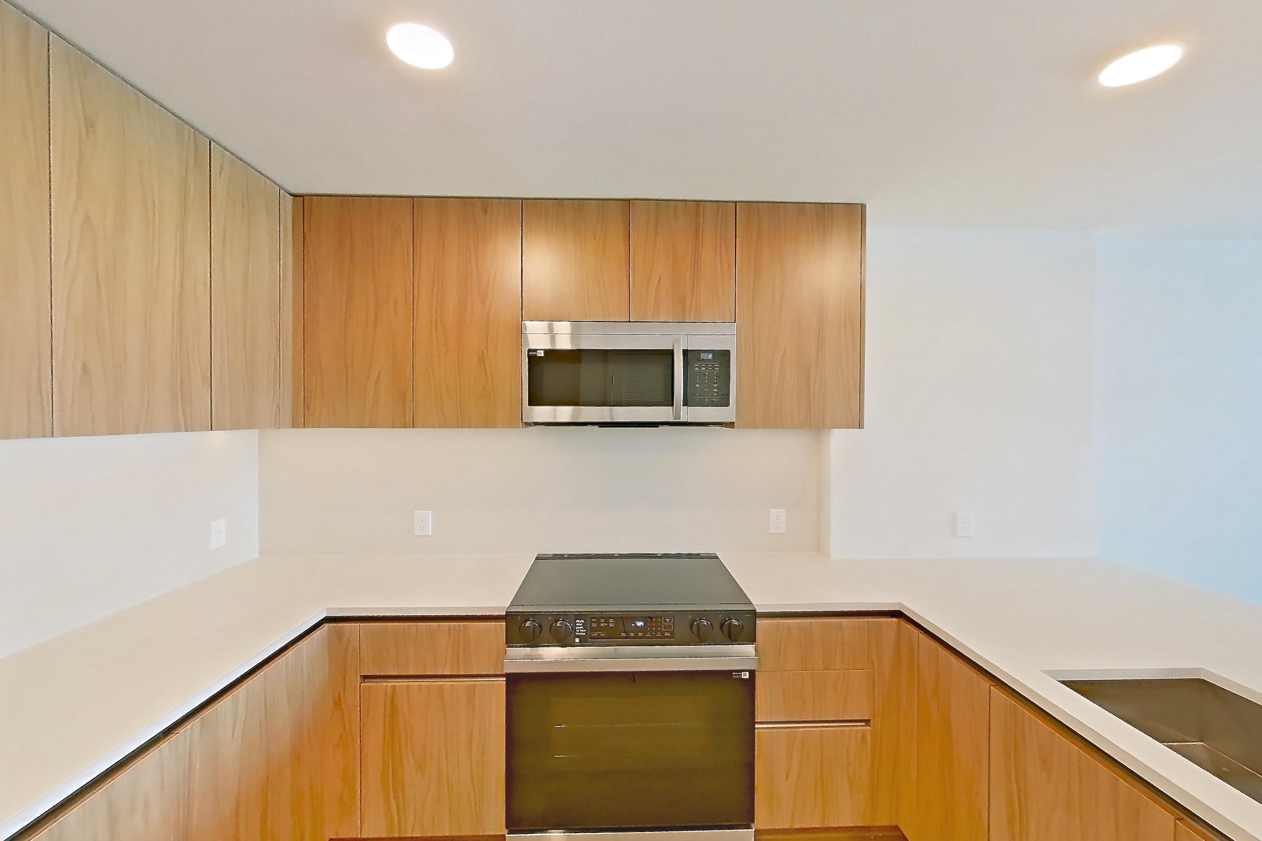 Kitchen with dishwasher, electric range, light countertops, light stone countertops, light wood-finish flooring, microwave, oven/range, refrigerator, and stainless steel appliances, Apartment 652 at Rowyn