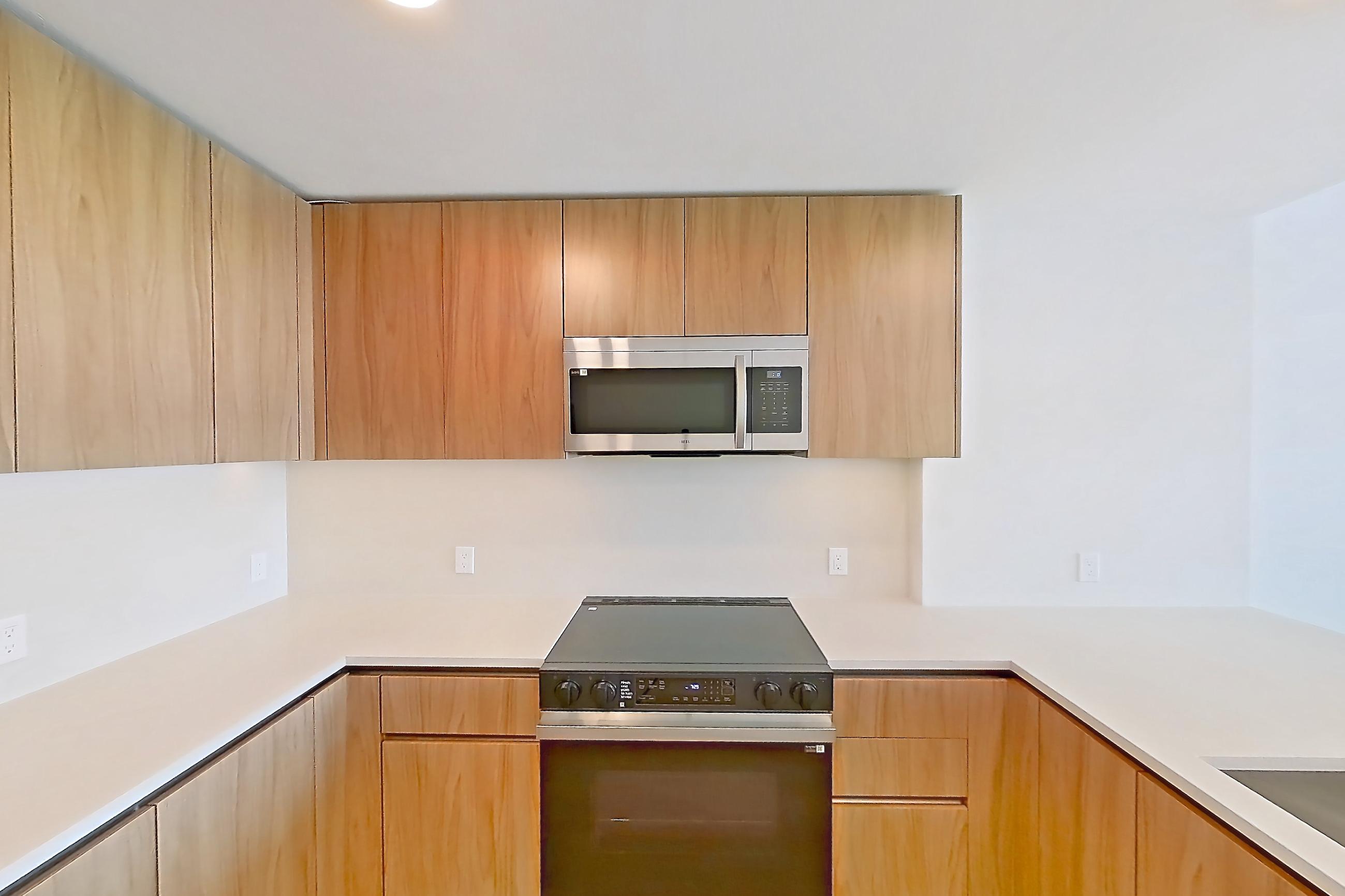Kitchen with dishwasher, electric range, kitchen island, light countertops, light stone countertops, light wood-finish flooring, microwave, oven/range, and stainless steel appliances, Apartment 855 at Rowyn