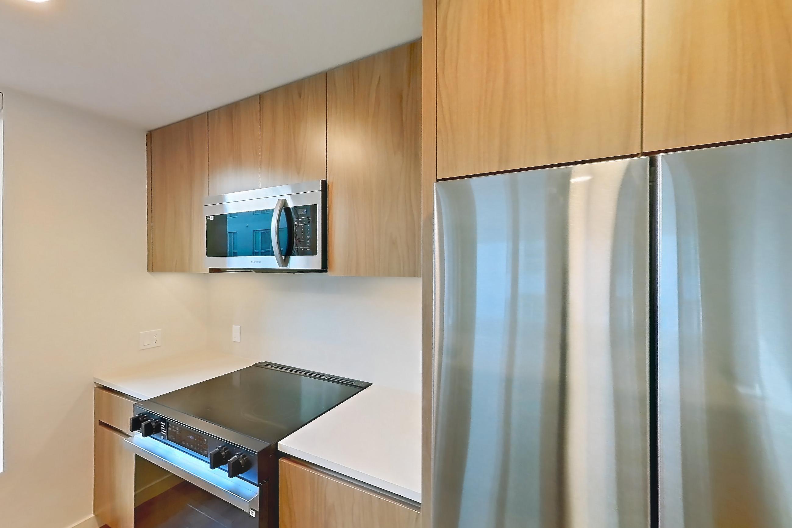 Kitchen with black appliances, dishwasher, electric range, light countertops, light wood-finish flooring, microwave, oven/range, refrigerator, and stainless steel appliances, Apartment 401 at Rowyn