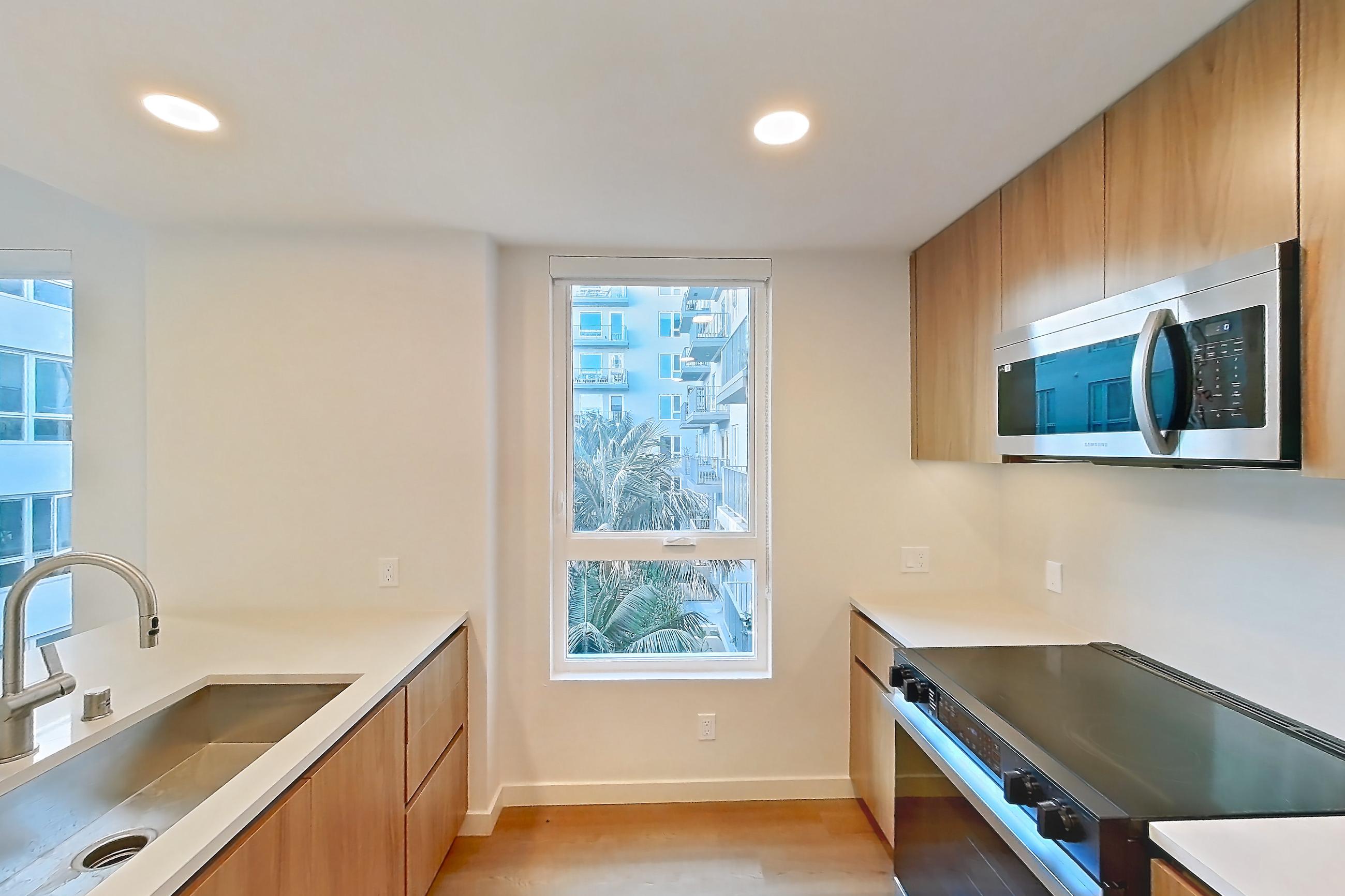 Kitchen with black appliances, dishwasher, electric range, light countertops, light wood-finish flooring, microwave, oven/range, refrigerator, and stainless steel appliances, Apartment 401 at Rowyn