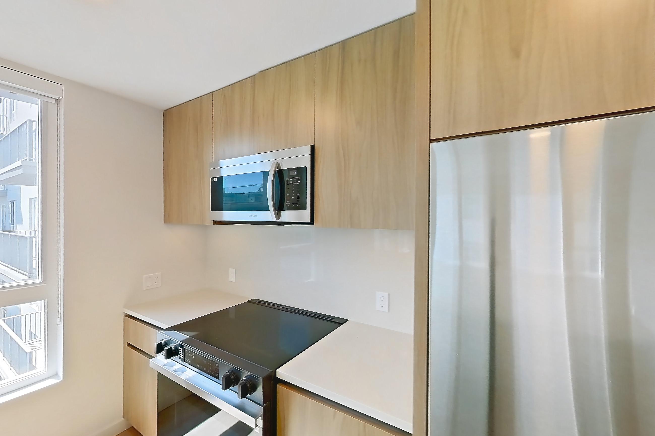Kitchen with dishwasher, electric range, light countertops, light stone countertops, light wood-finish flooring, oven/range, refrigerator, and stainless steel appliances, Apartment 601 at Rowyn