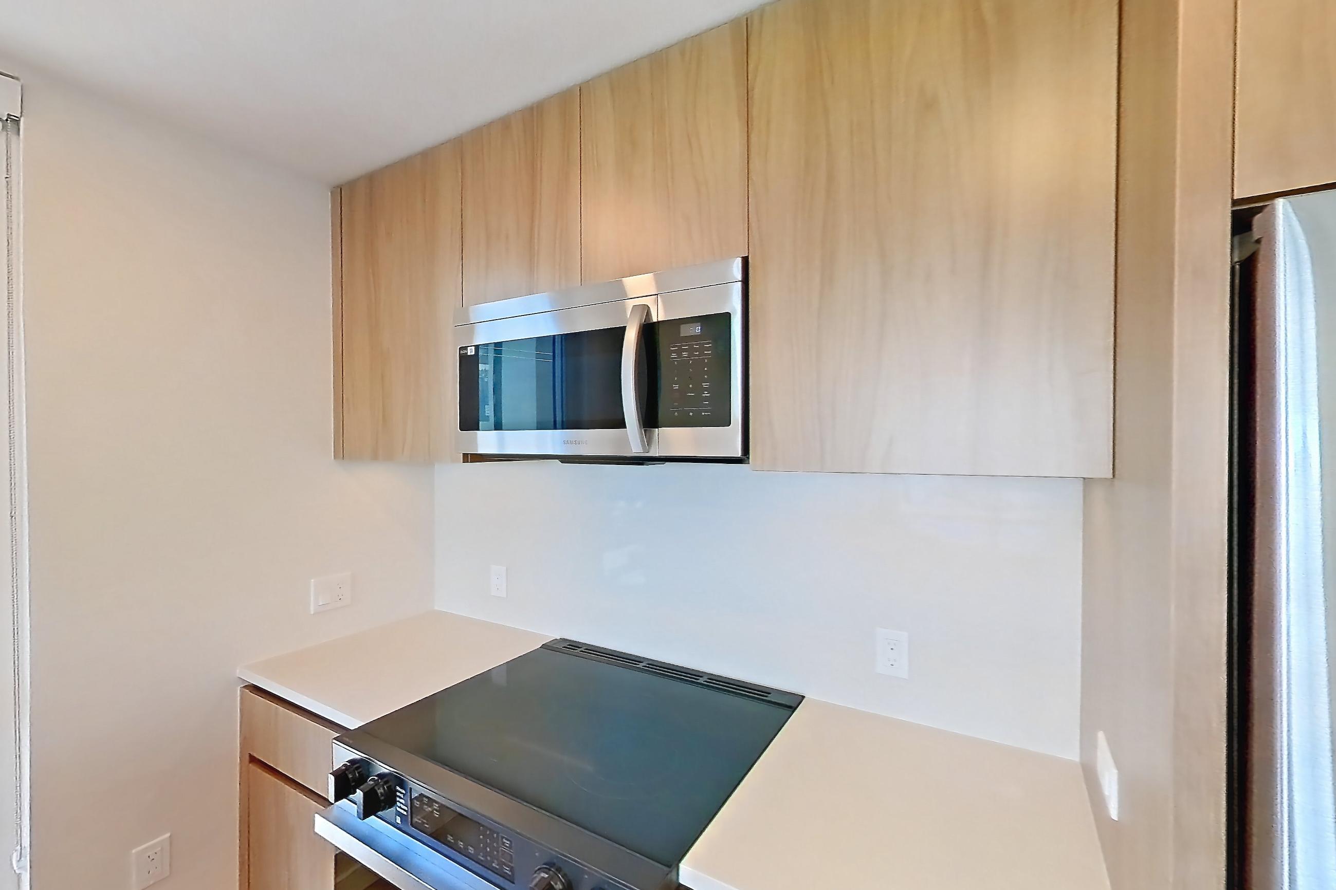 Kitchen with dishwasher, electric range, kitchen island, light countertops, light stone countertops, light wood-finish flooring, microwave, oven/range, refrigerator, and stainless steel appliances, Apartment 404 at Rowyn