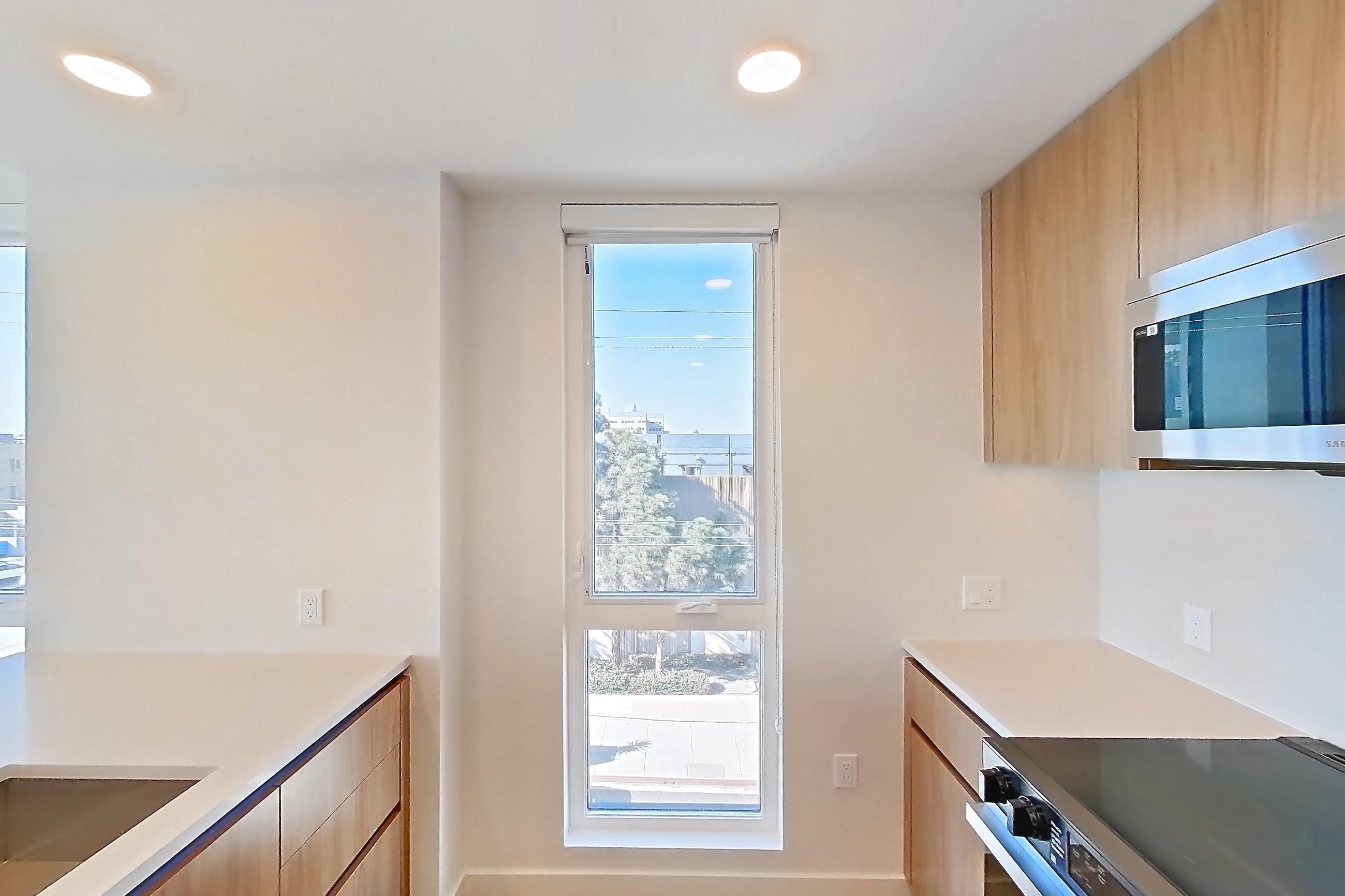 Kitchen with dishwasher, electric range, kitchen island, light countertops, light stone countertops, light wood-finish flooring, microwave, oven/range, refrigerator, and stainless steel appliances, Apartment 404 at Rowyn