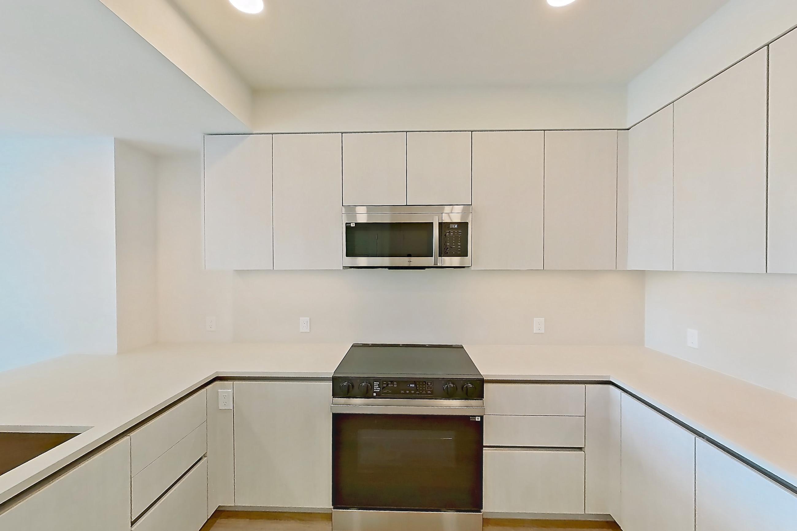 Kitchen with dishwasher, electric range, light countertops, light stone countertops, light wood-finish flooring, microwave, oven/range, refrigerator, and stainless steel appliances, Apartment 339 at Rowyn