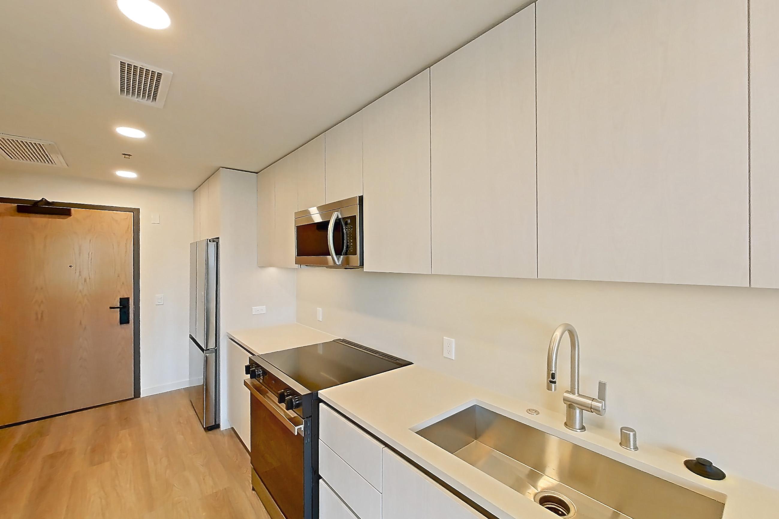 Kitchen with dishwasher, electric range, light countertops, light wood-finish flooring, microwave, oven/range, refrigerator, and stainless steel appliances, Apartment 325 at Rowyn