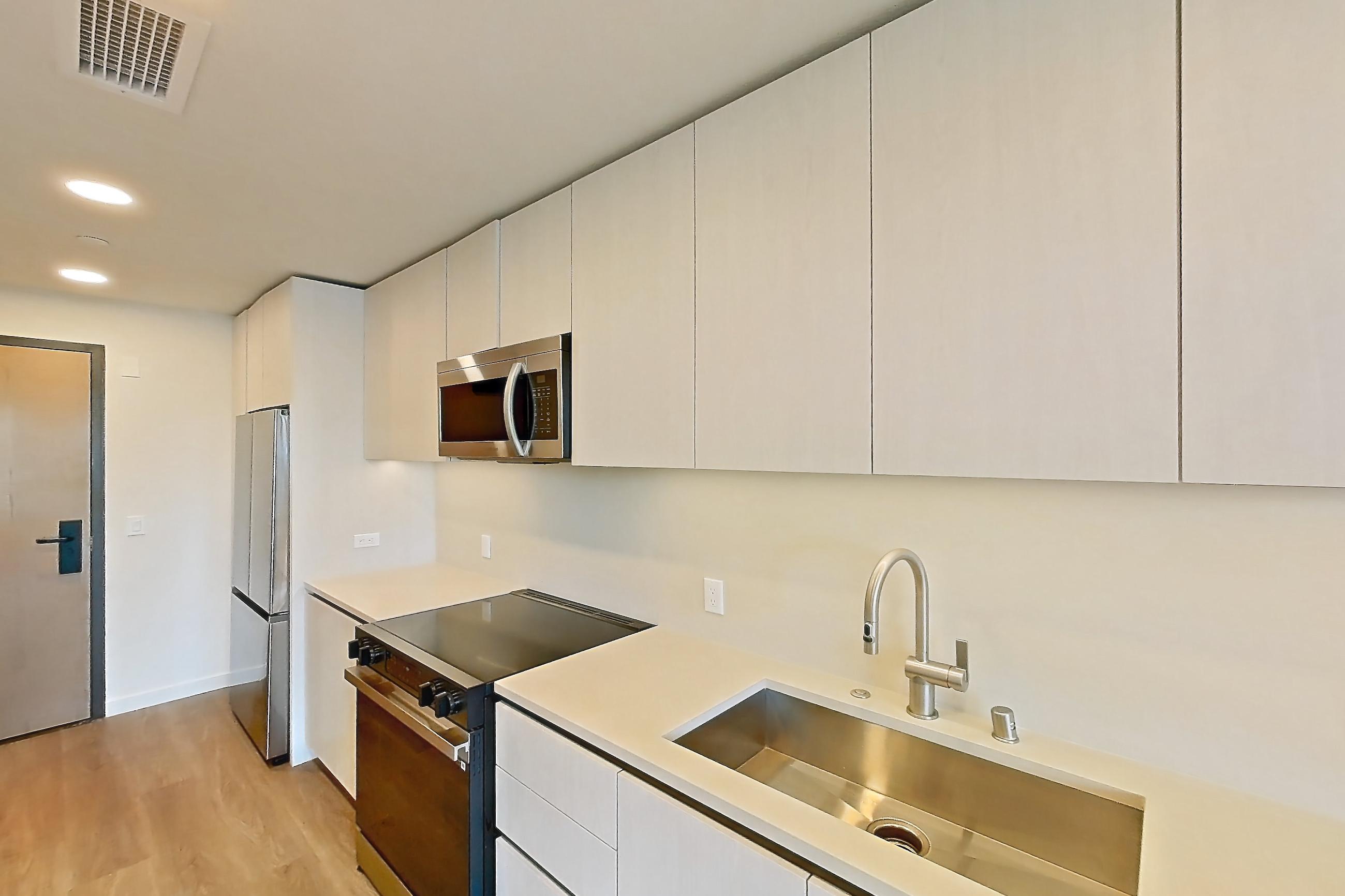 Kitchen with black appliances, dishwasher, electric range, light countertops, light wood-finish flooring, microwave, oven/range, refrigerator, and stainless steel appliances, Apartment 329 at Rowyn