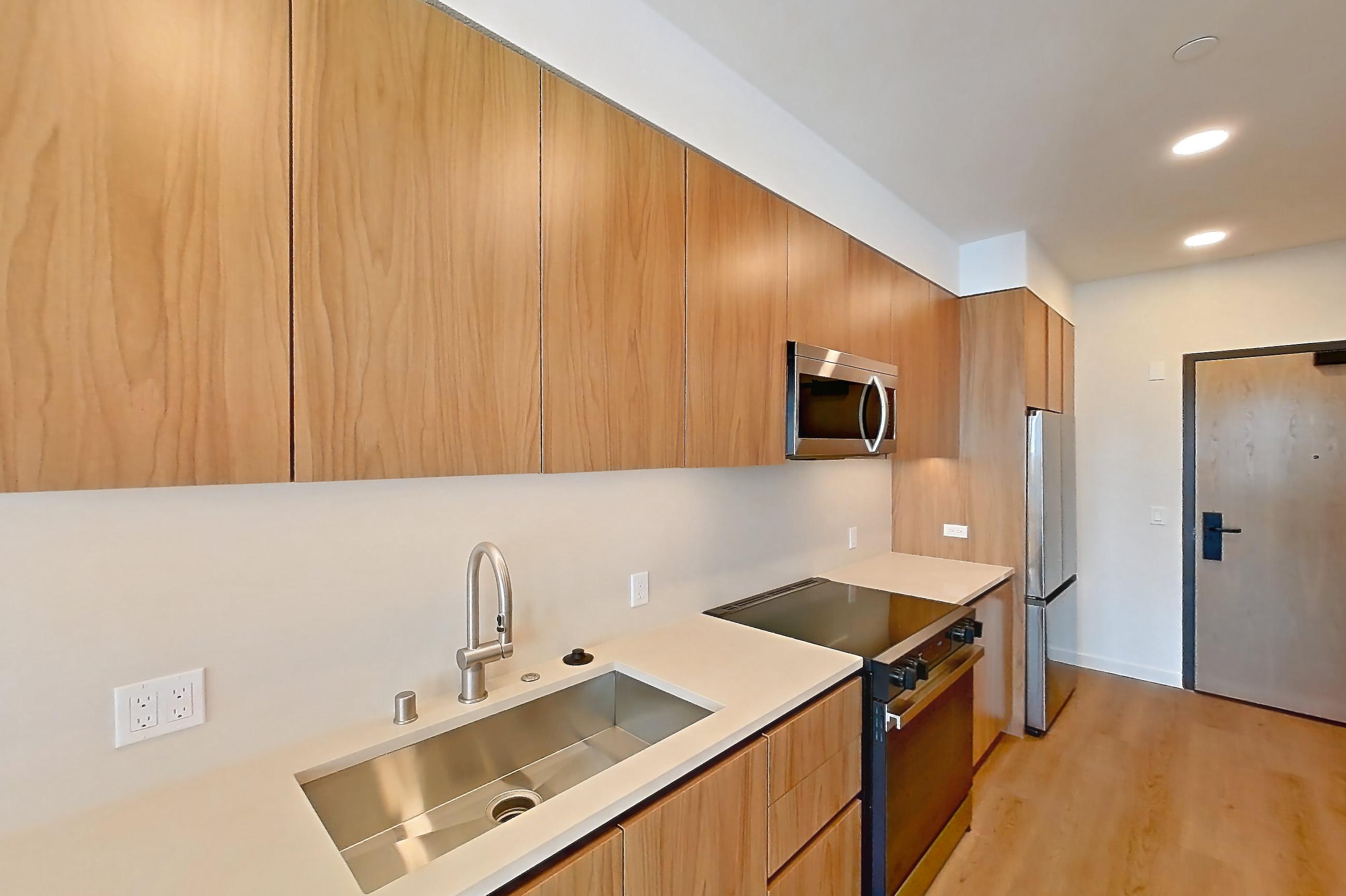 Kitchen with dishwasher, electric range, light countertops, light stone countertops, light wood-finish flooring, oven/range, refrigerator, and stainless steel appliances, Apartment 423 at Rowyn