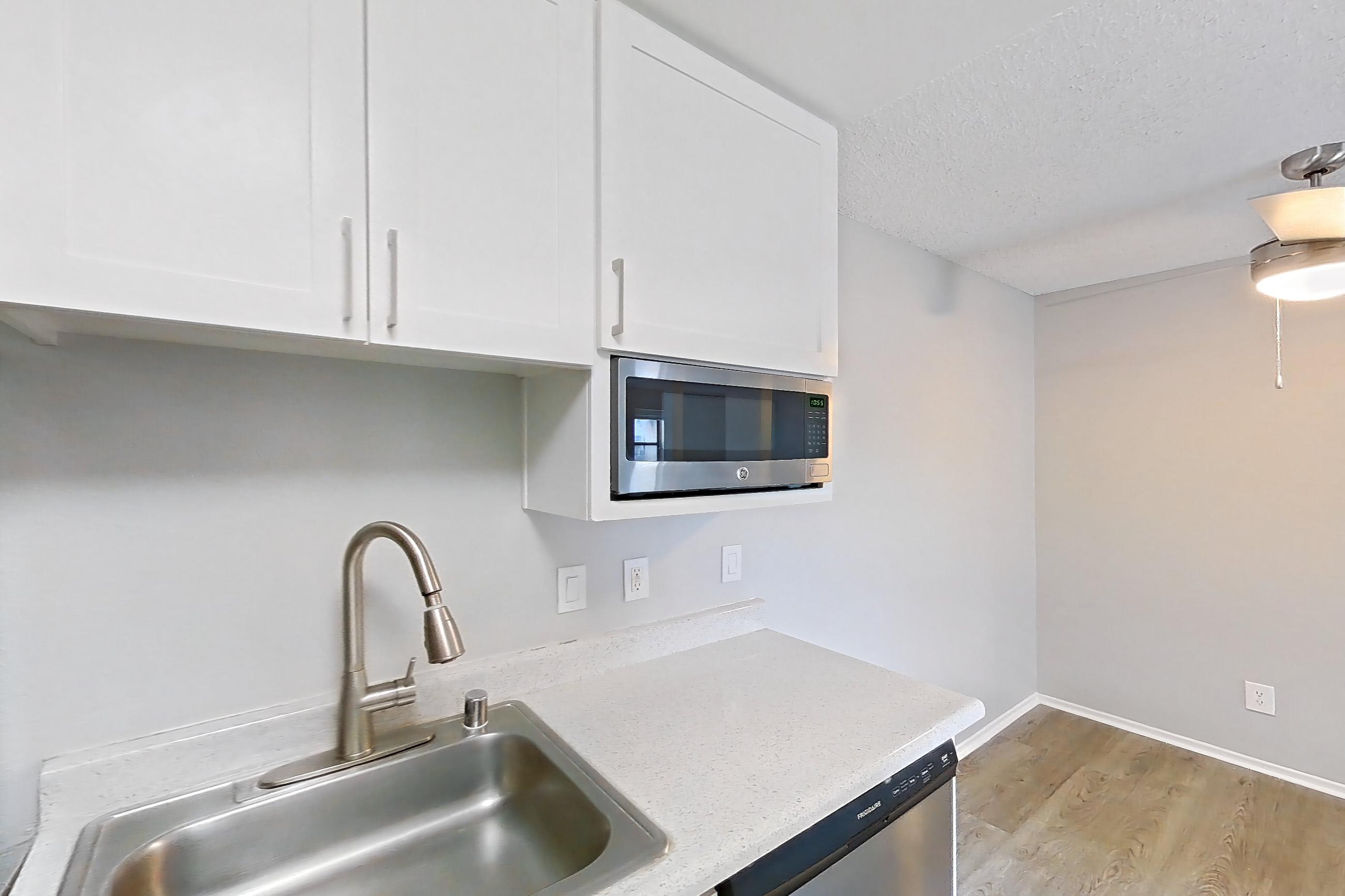Kitchen with dishwasher, electric range, light countertops, light stone countertops, light wood-finish flooring, oven/range, range hood, refrigerator, and stainless steel appliances, Apartment 06-08 at Avana Rancho Cucamonga