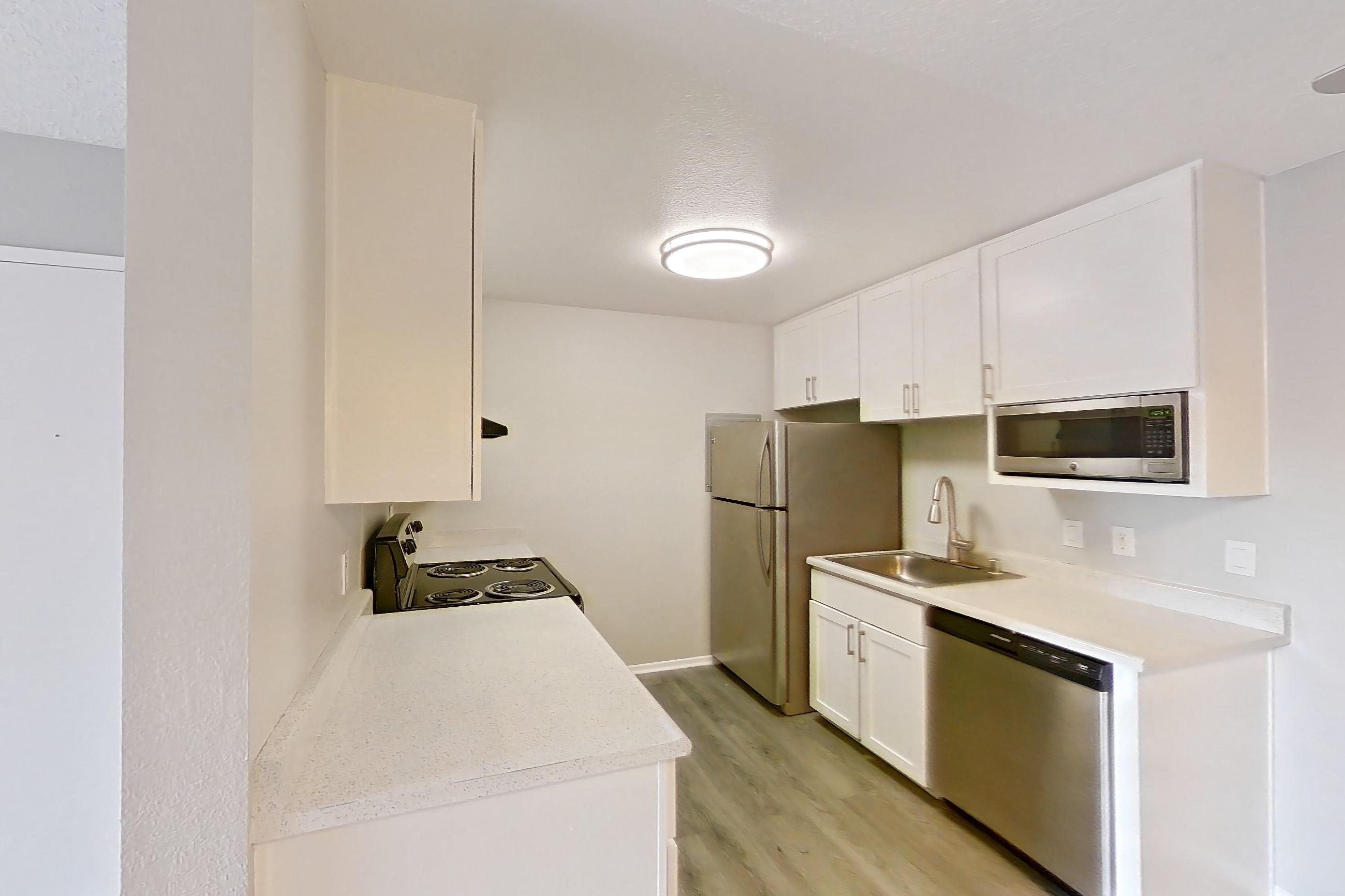 Living space with black appliances, dishwasher, electric range, light countertops, light wood-finish flooring, oven/range, refrigerator, stainless steel appliances, and white appliances, Apartment 06-08 at Avana Rancho Cucamonga