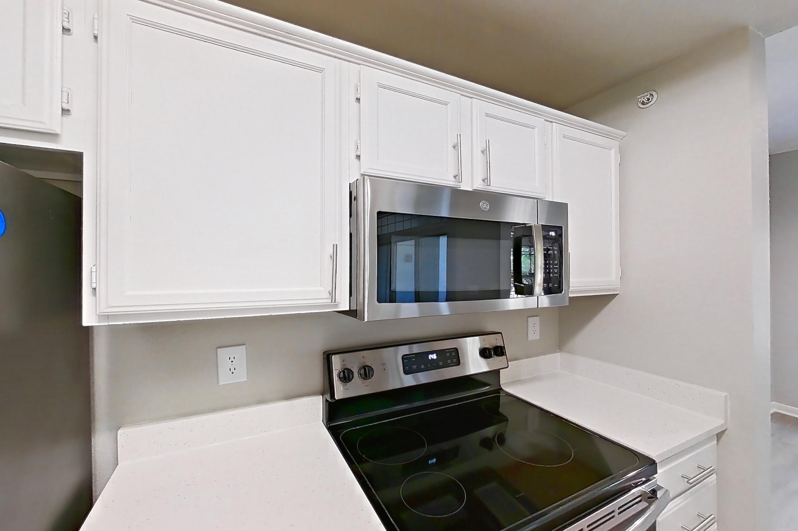 Kitchen with dishwasher, electric range, light countertops, light stone countertops, light wood-finish flooring, microwave, oven/range, refrigerator, and stainless steel appliances, Unit 307 at Riviera at West Village