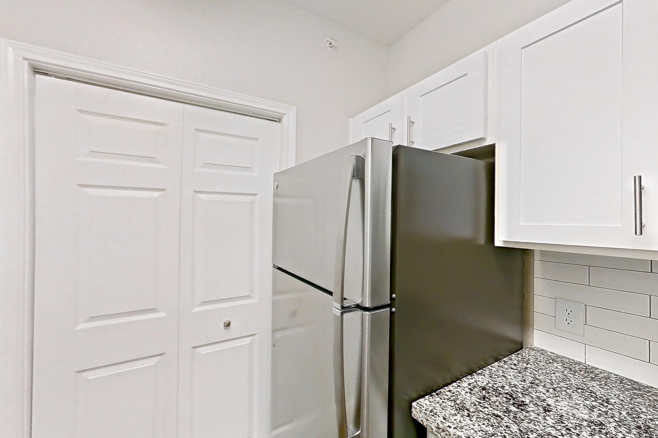 Kitchen with dark carpet, dark wood-finish flooring, dishwasher, electric range, glass shower door, light countertops, light stone countertops, light wood-finish flooring, oven/range, refrigerator, stainless steel appliances, stall shower, walk-in shower, and white appliances, Apartment 0222 at Reserve at Kingwood