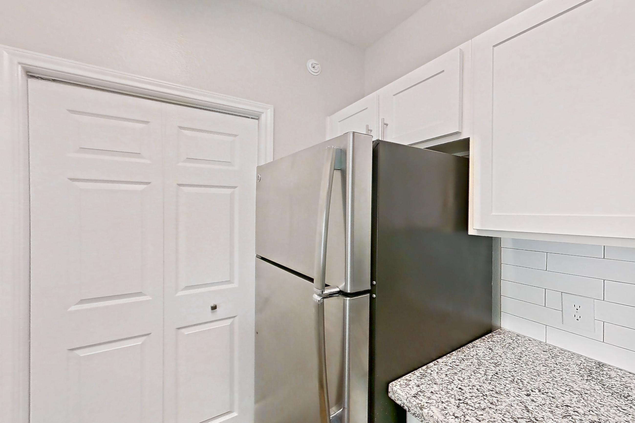 Kitchen with dark wood-finish flooring, dishwasher, electric range, light carpet, light countertops, light stone countertops, light wood-finish flooring, oven/range, refrigerator, stainless steel appliances, and wood-finish flooring, Apartment 0737 at Reserve at Kingwood