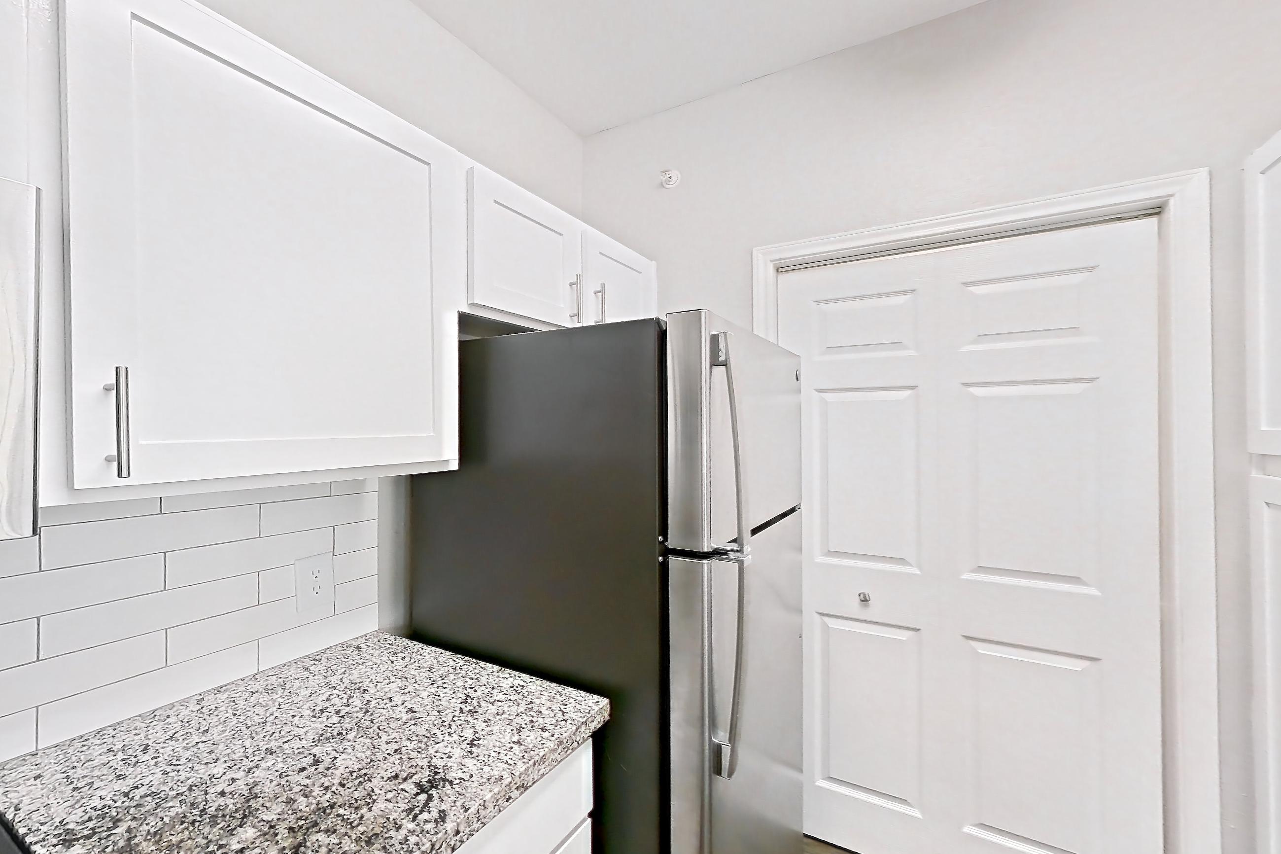 Kitchen with dark carpet, dark wood-finish flooring, dishwasher, electric range, light countertops, light stone countertops, oven/range, refrigerator, and stainless steel appliances, Apartment 0632 at Reserve at Kingwood