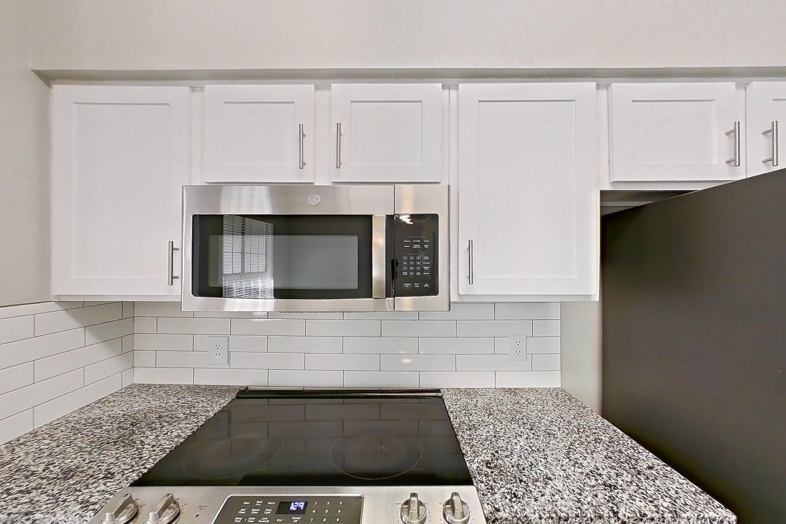 Kitchen with dark wood-finish flooring, dishwasher, electric range, light carpet, light countertops, light stone countertops, light wood-finish flooring, oven/range, refrigerator, and stainless steel appliances, Apartment 0535 at Reserve at Kingwood