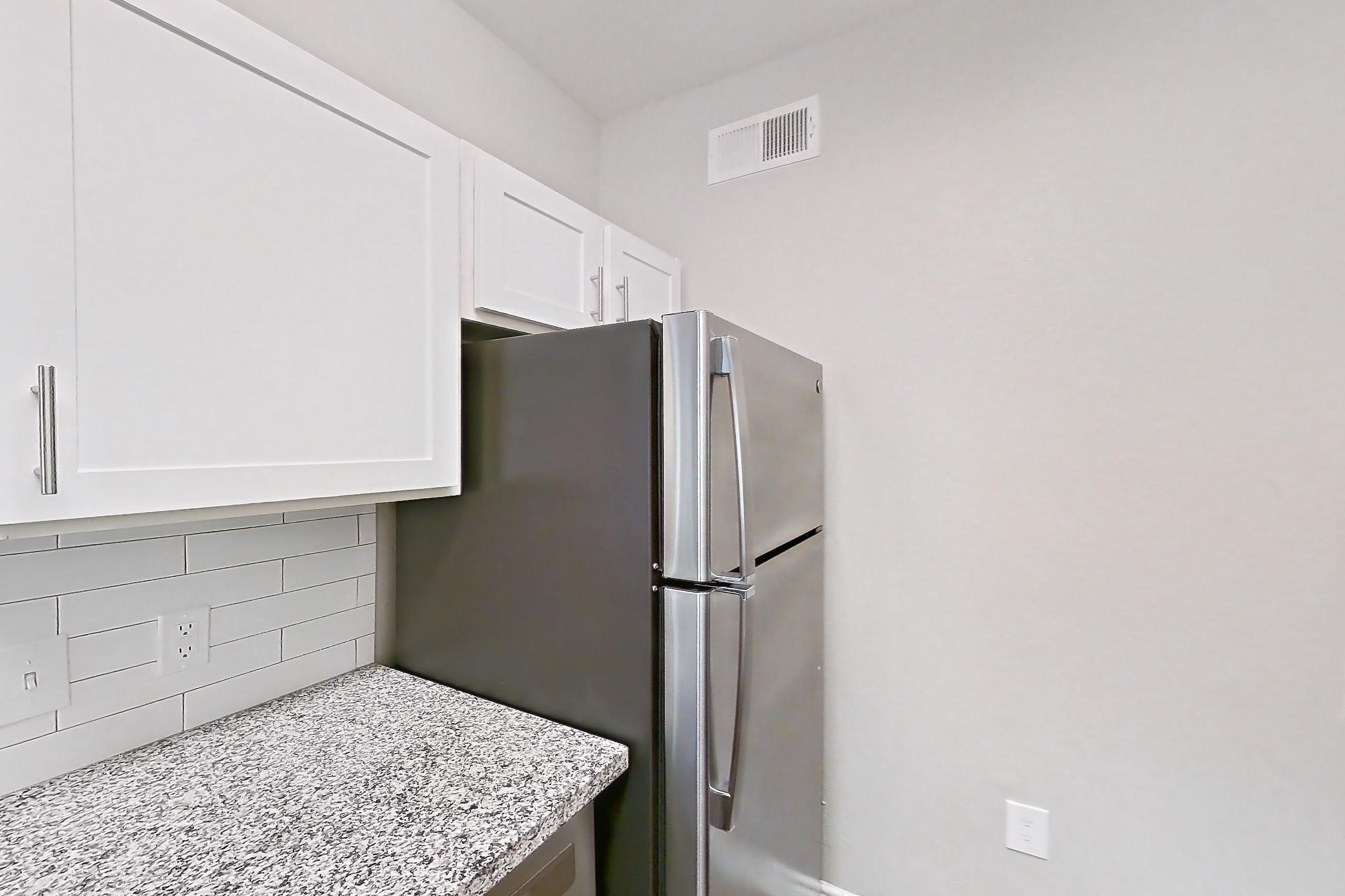 Kitchen with dark carpet, dark wood-finish flooring, dishwasher, electric range, light countertops, light stone countertops, microwave, oven/range, refrigerator, stainless steel appliances, and white appliances, Apartment 0529 at Reserve at Kingwood