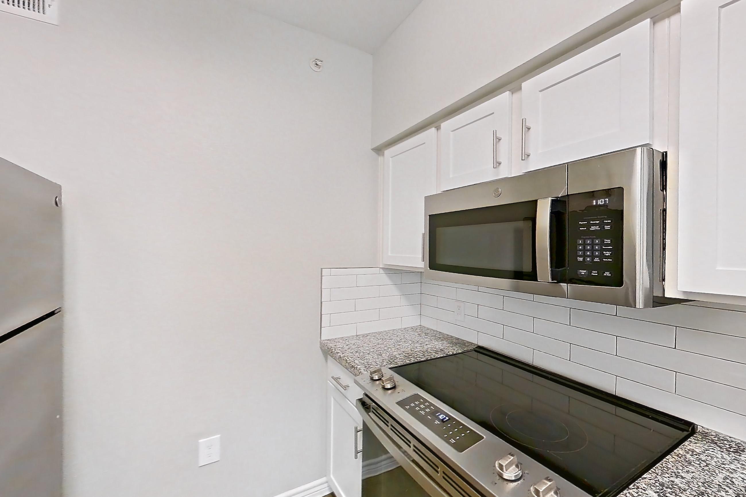 Kitchen with dark carpet, dark wood-finish flooring, dishwasher, electric range, light countertops, light stone countertops, microwave, oven/range, refrigerator, stainless steel appliances, and white appliances, Apartment 0529 at Reserve at Kingwood