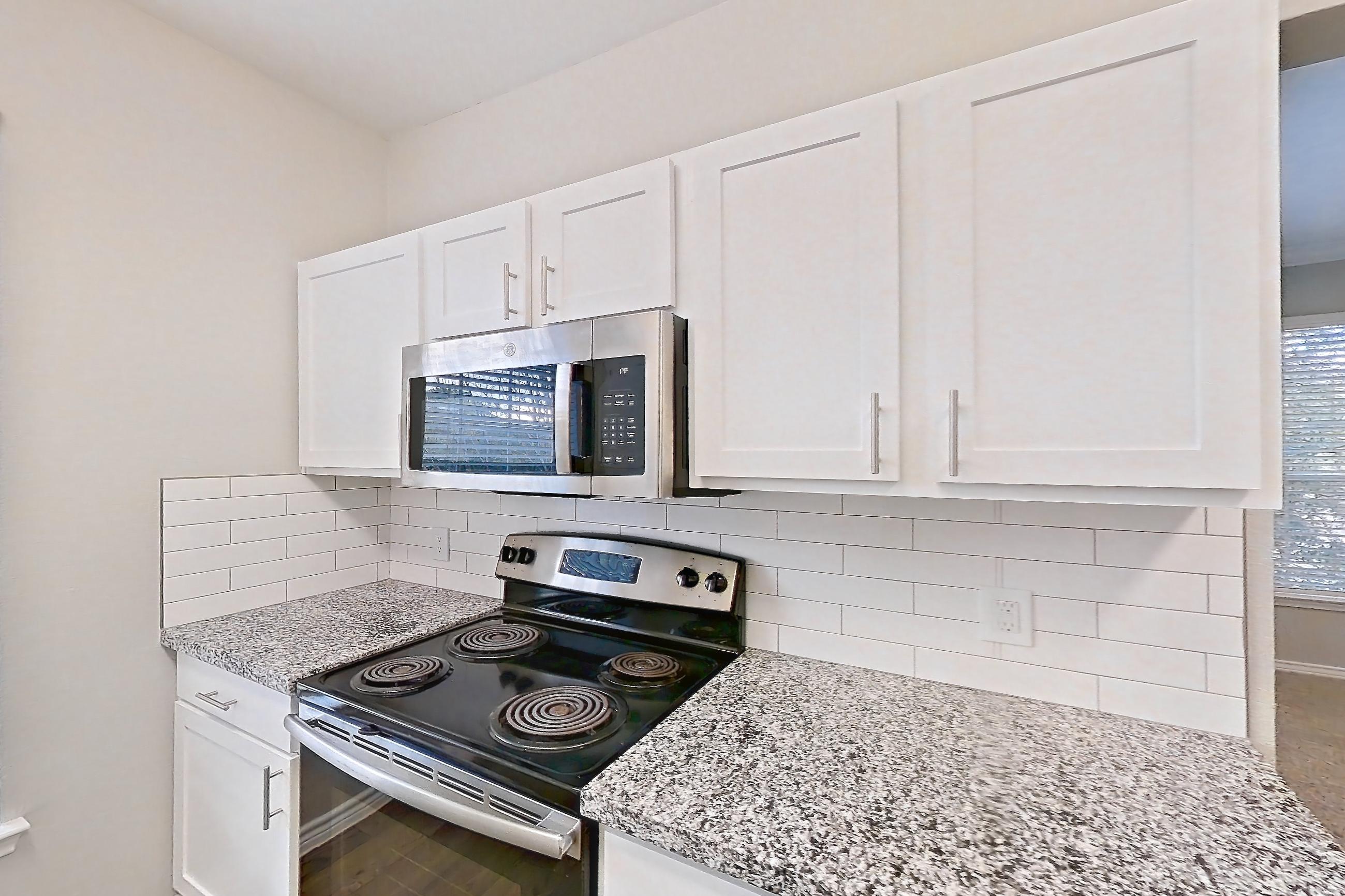 Kitchen with dishwasher, electric range, light carpet, light countertops, light stone countertops, light wood-finish flooring, microwave, oven/range, refrigerator, and stainless steel appliances, Apartment 1031 at Reserve at Kingwood