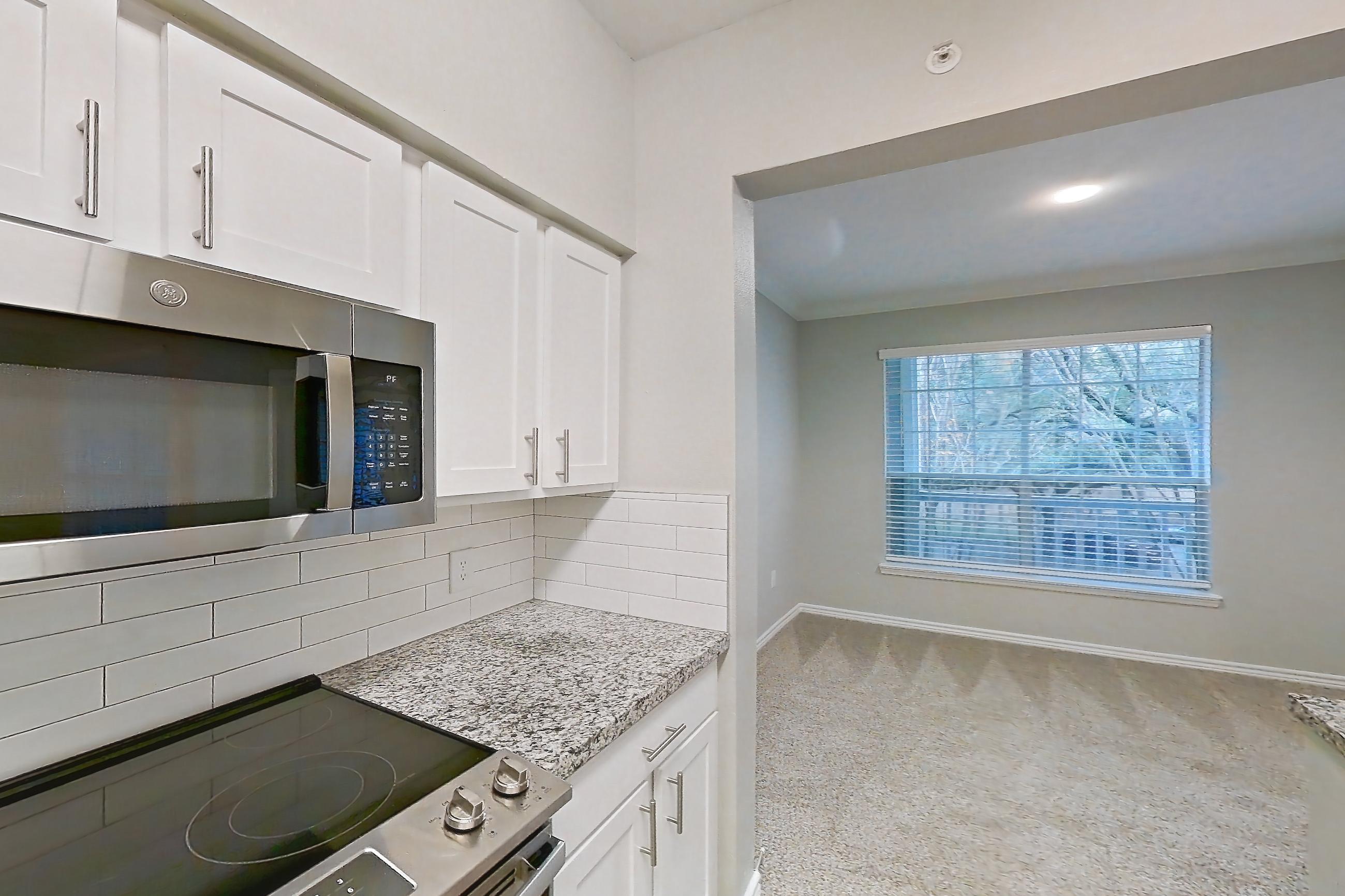 Kitchen with dark carpet, dark wood-finish flooring, dishwasher, electric range, light countertops, light stone countertops, oven/range, refrigerator, and stainless steel appliances, Apartment 1122 at Reserve at Kingwood