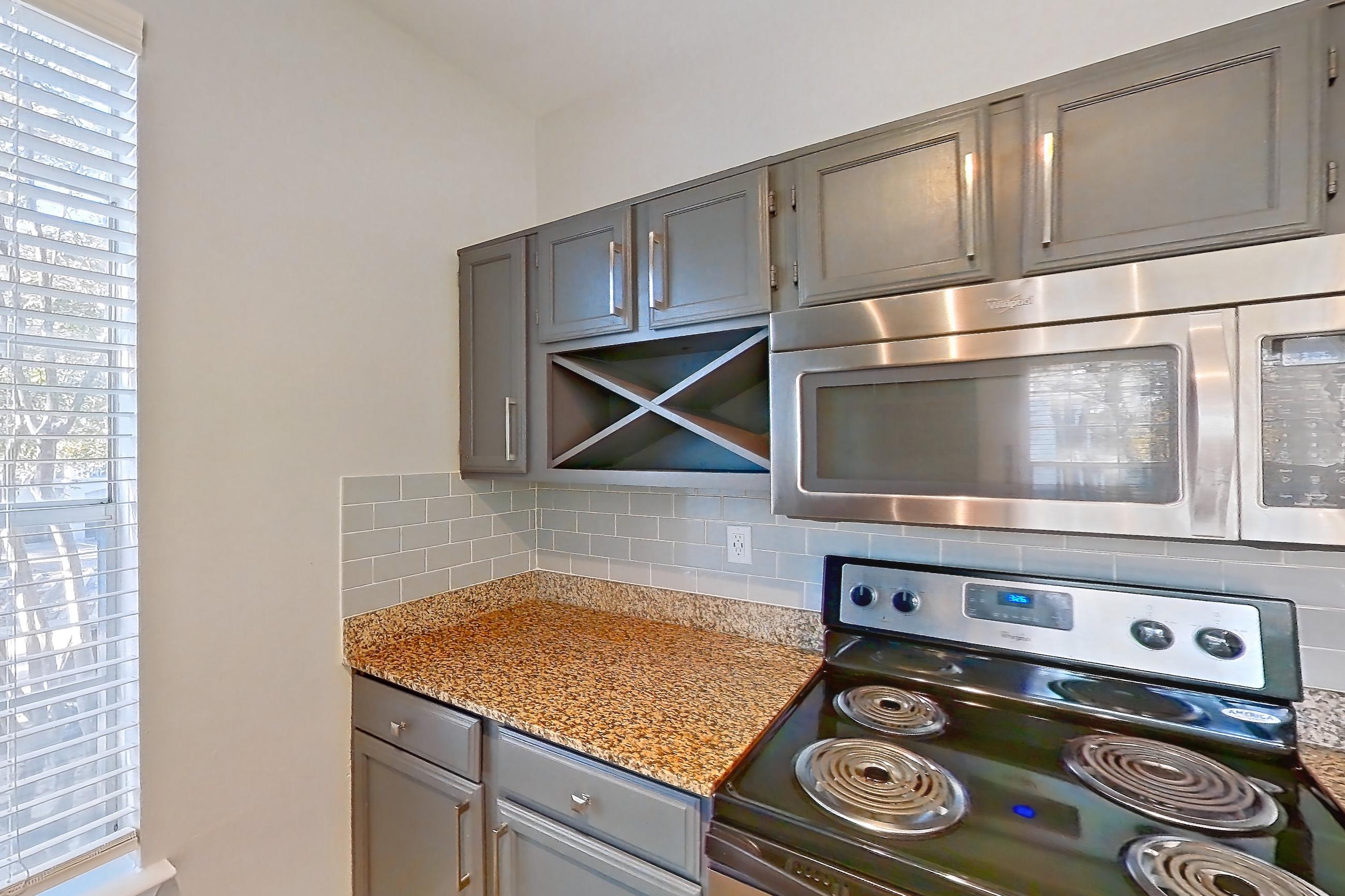 Kitchen with dark countertops, dishwasher, electric range, light carpet, light countertops, light stone countertops, light wood-finish flooring, microwave, oven/range, refrigerator, and stainless steel appliances, Apartment 0327 at Marquis Champions Forest