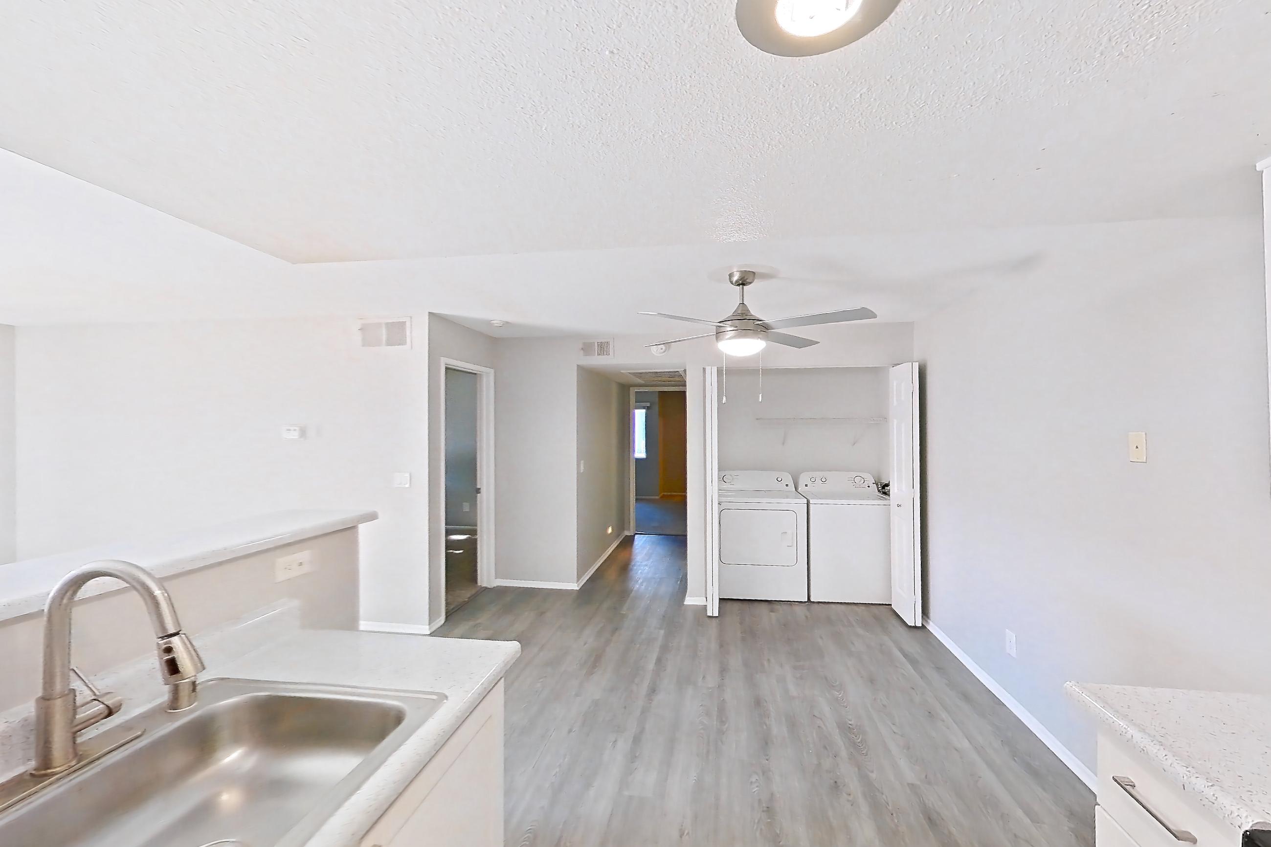 Kitchen with dishwasher, electric range, in-unit laundry, light countertops, light stone countertops, light wood-finish flooring, microwave, oven/range, refrigerator, and stainless steel appliances, Apartment Z-05 at Avana Rancho Cucamonga