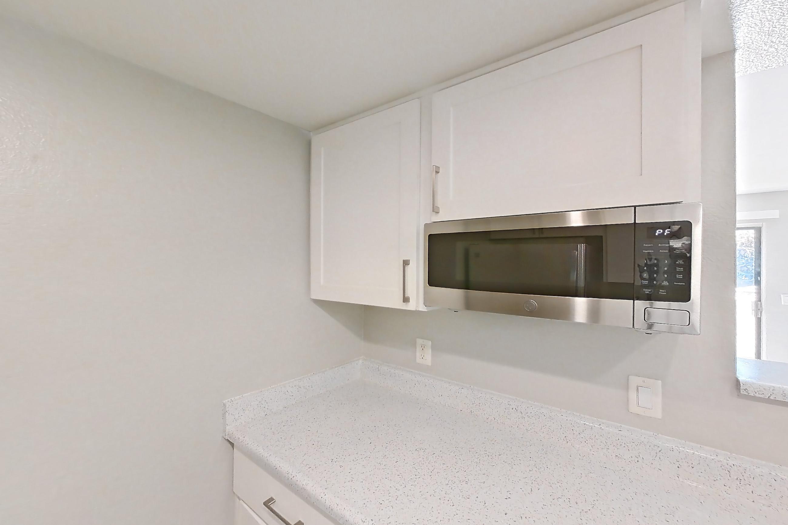 Kitchen with dishwasher, electric range, in-unit laundry, light countertops, light stone countertops, light wood-finish flooring, microwave, oven/range, refrigerator, and stainless steel appliances, Apartment Z-05 at Avana Rancho Cucamonga