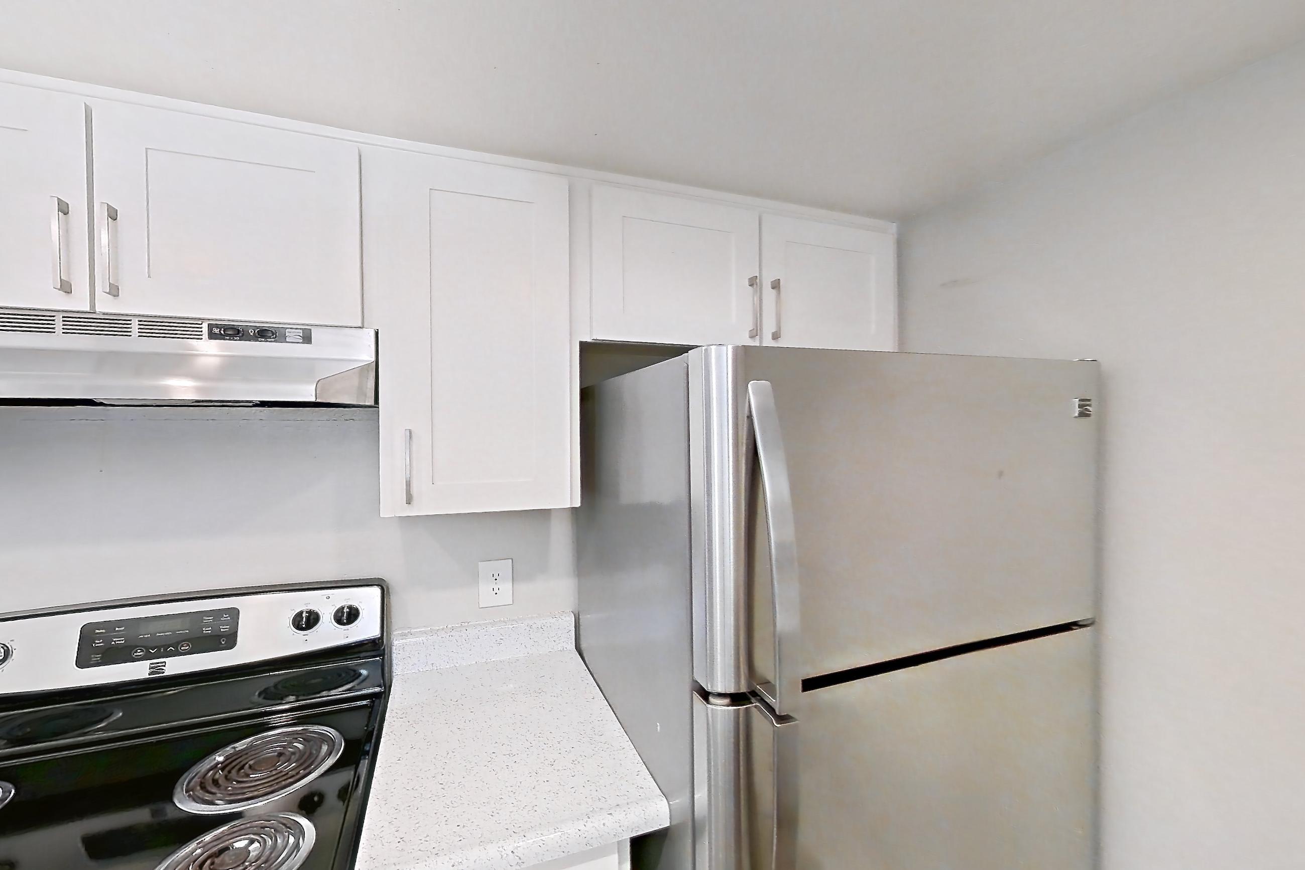 Kitchen with dishwasher, electric range, in-unit laundry, light countertops, light stone countertops, light wood-finish flooring, microwave, oven/range, refrigerator, and stainless steel appliances, Apartment Z-05 at Avana Rancho Cucamonga