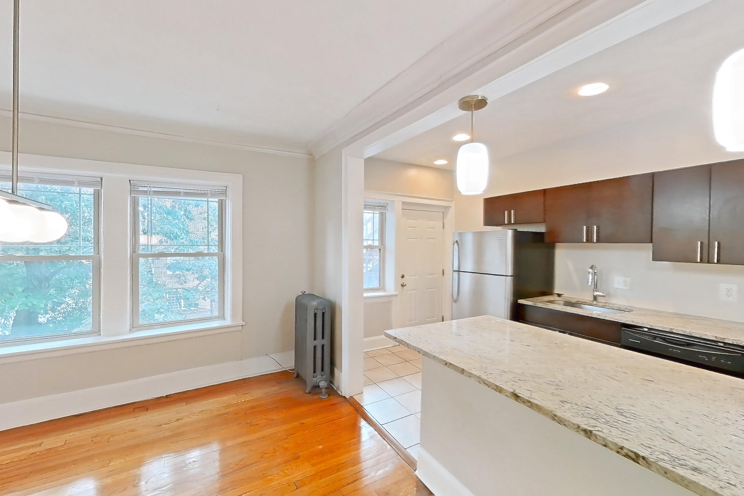 Dining room with black appliances, dishwasher, gas range, light countertops, light stone countertops, light wood-finish flooring, oven/range, radiator heat, refrigerator, stainless steel appliances, and wood-finish flooring, Apartment 48-04 at Integrity Cleveland Heights