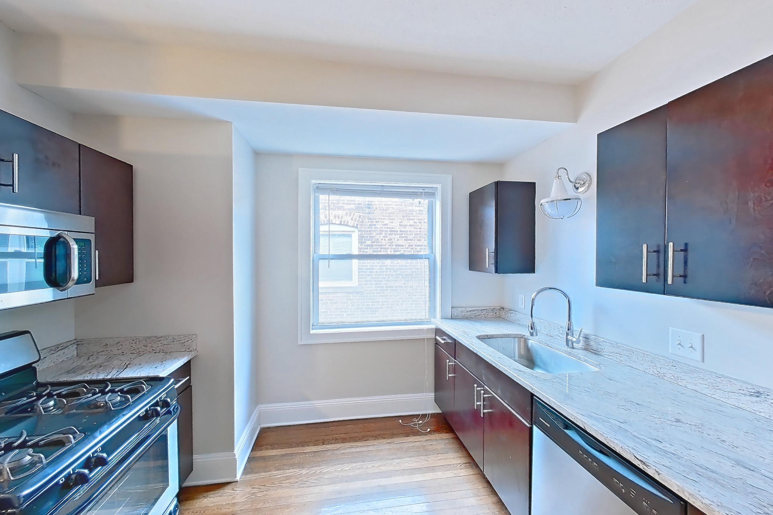 Kitchen with dark wood-finish flooring, dishwasher, gas range, light countertops, light stone countertops, light wood-finish flooring, microwave, oven/range, refrigerator, and stainless steel appliances, Apartment 5 at Integrity Cleveland Heights 